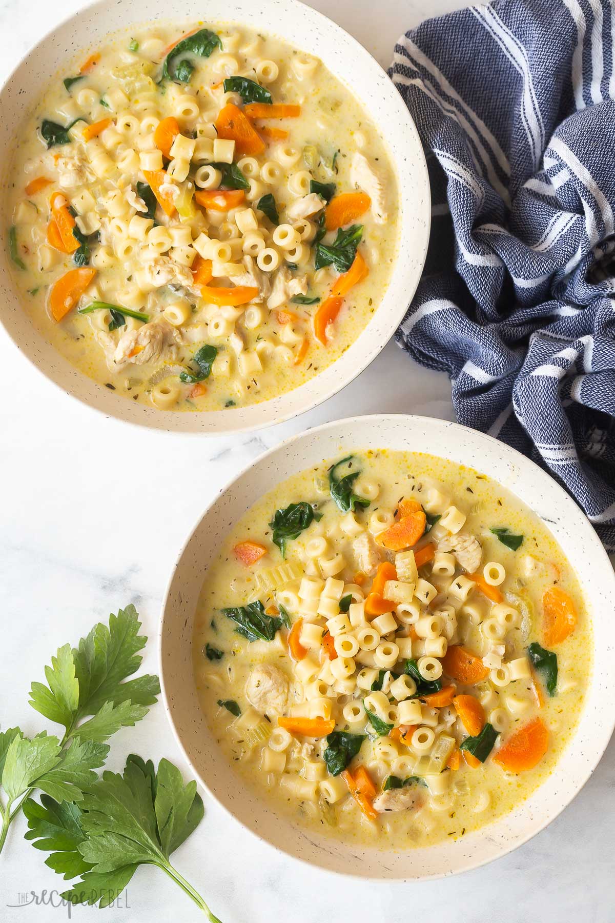 two bowls of instant pot chicken noodle soup with fresh parsley and blue towel.