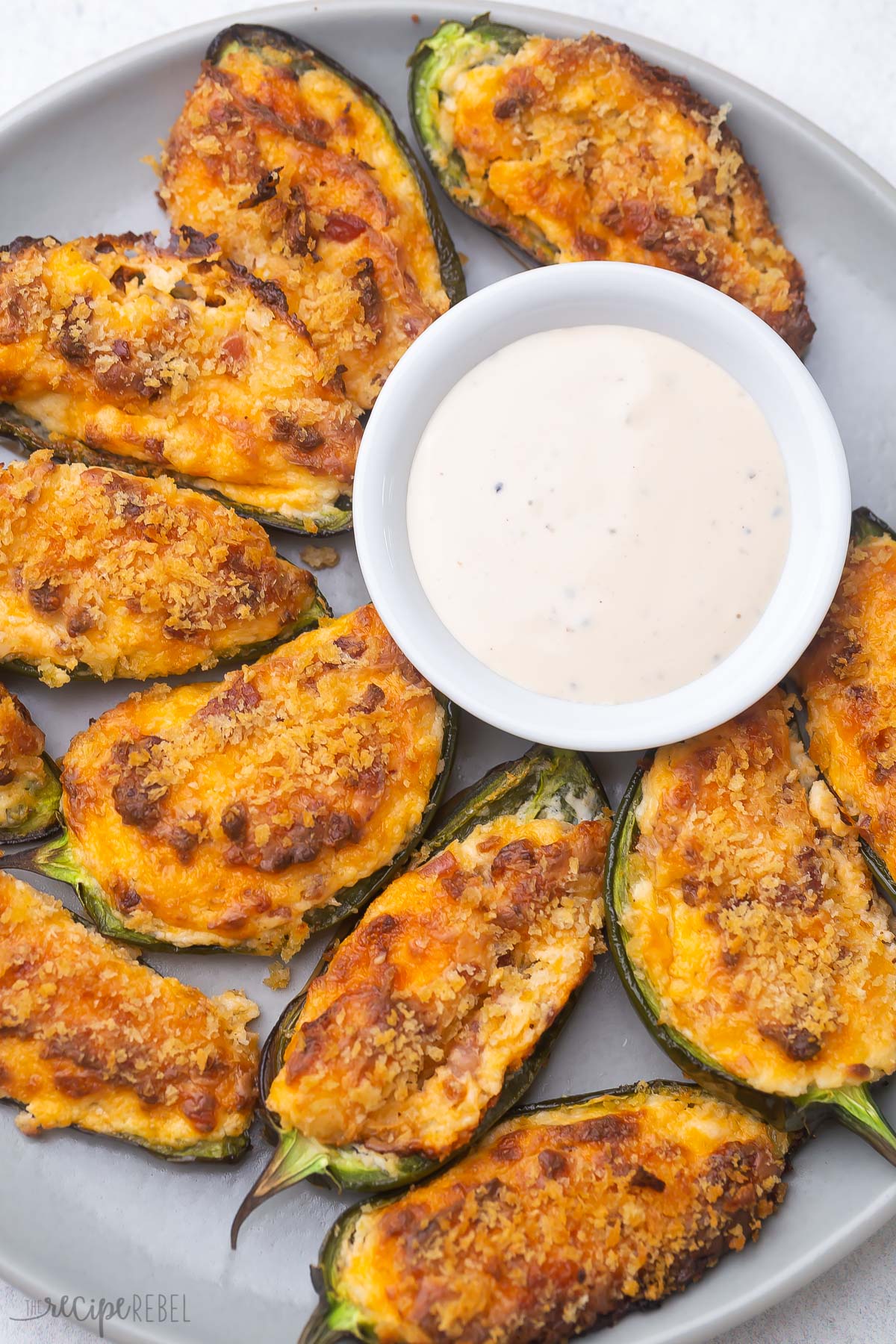 jalapeno poppers on parchment paper with a white bowl of dip.