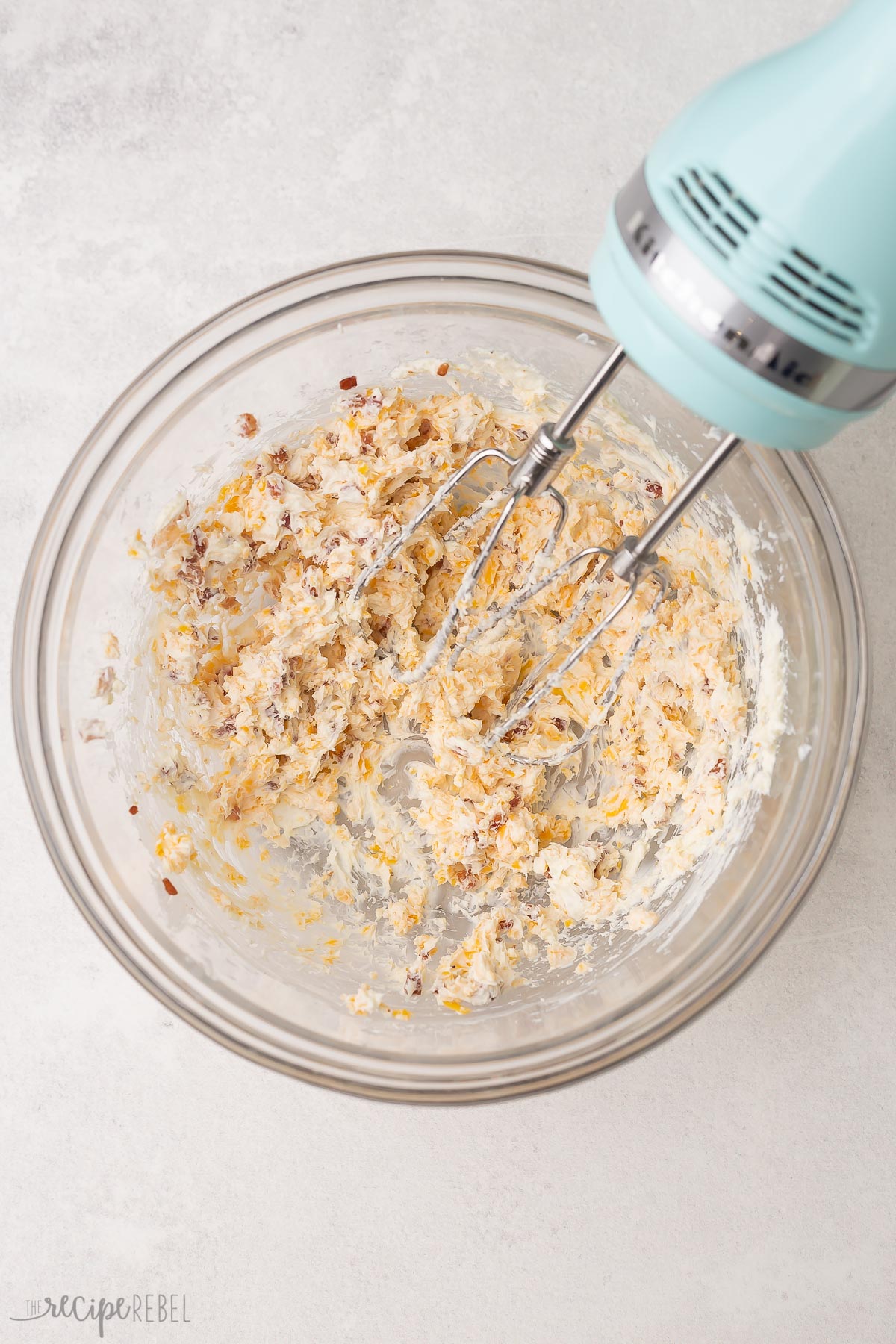 electric mixer mixing cream cheese ingredients in glass bowl.