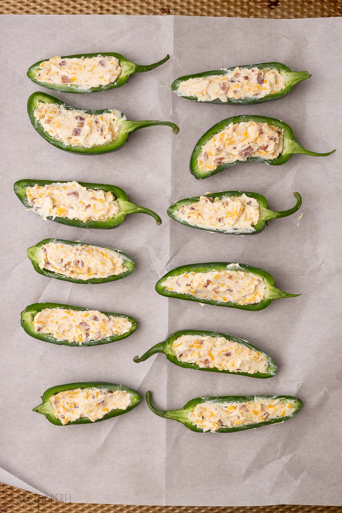 jalapenos with filling on a pan with parchment paper.