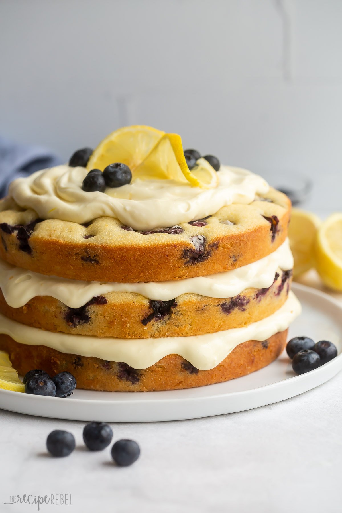 Side view of decorated lemon blueberry cake topped with lemon slices and blueberries.