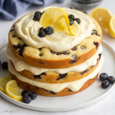 close up of lemon blueberry cake on white plate with lemon slices and blueberries on top.