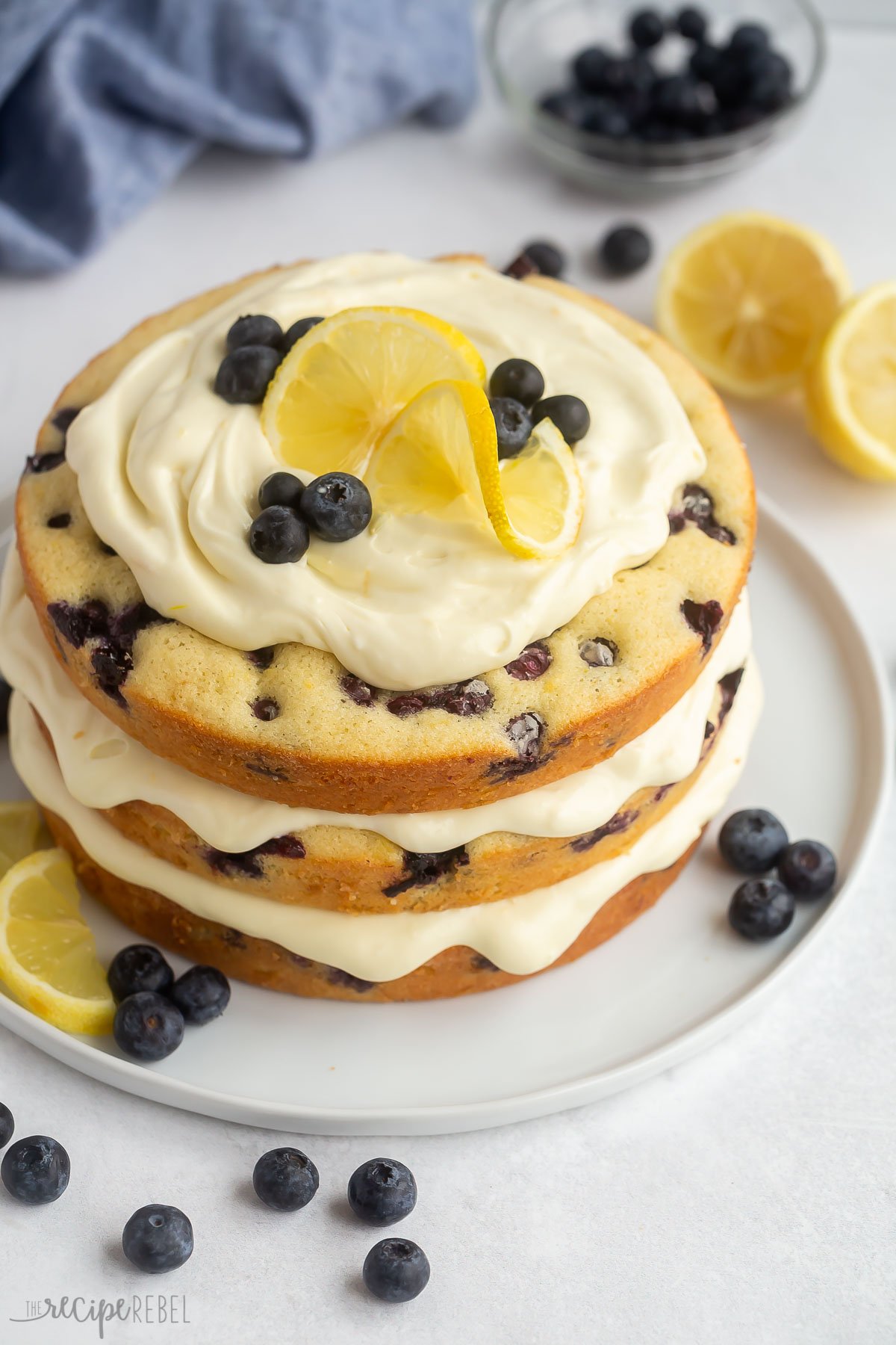 lemon blueberry cake on a white plate topped with lemon slices and blueberries.