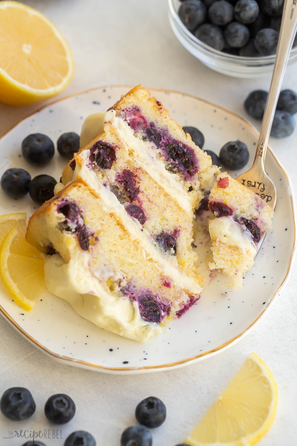 Top view of a slice of lemon blueberry cake on plate with fork and berries beside.