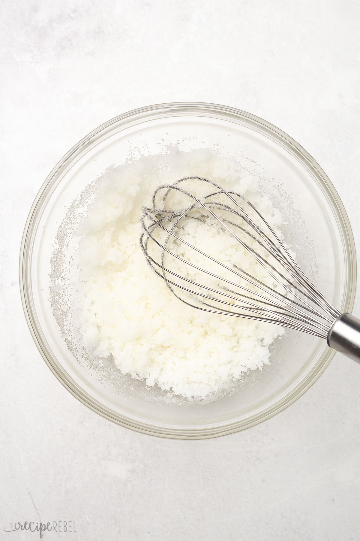 Top view of glass bowl with sugar, oil, and steel whisk.