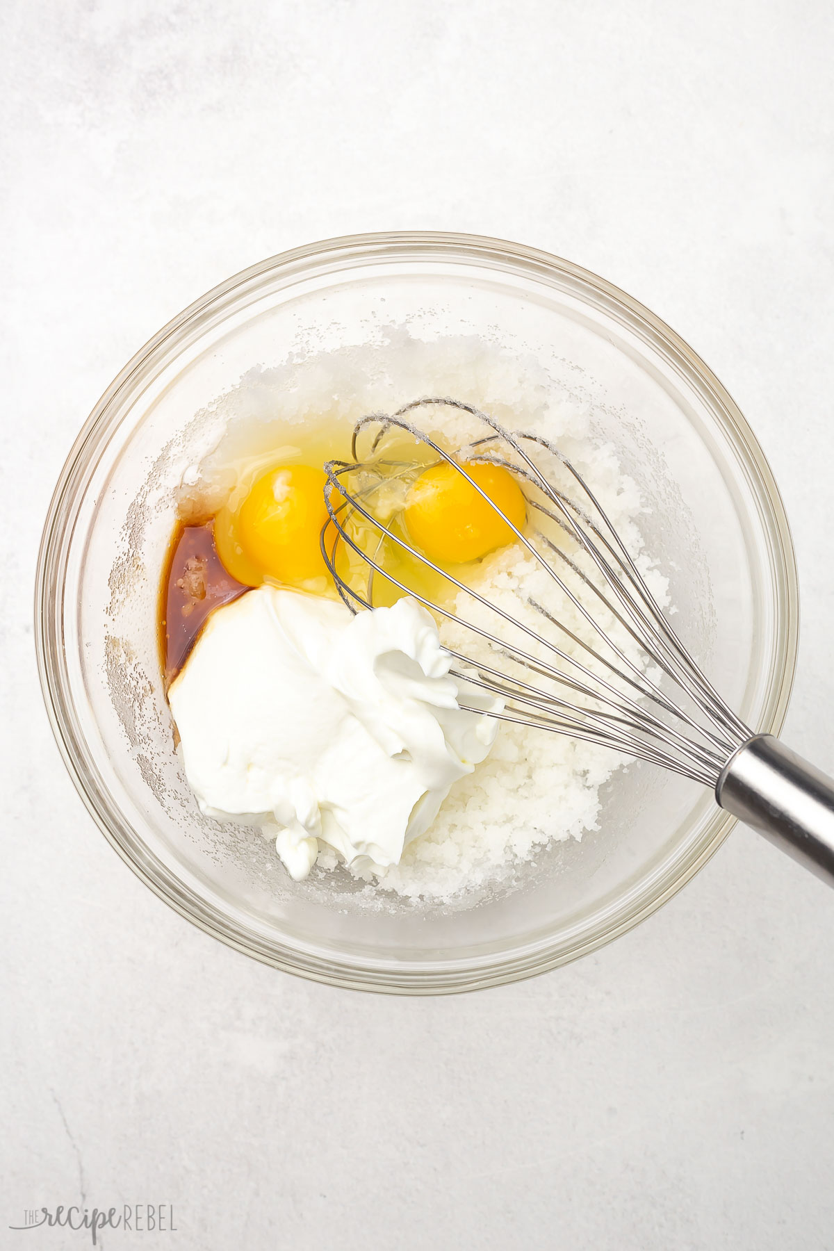 Top view of glass mixing bowl with wet ingredients and steel whisk.