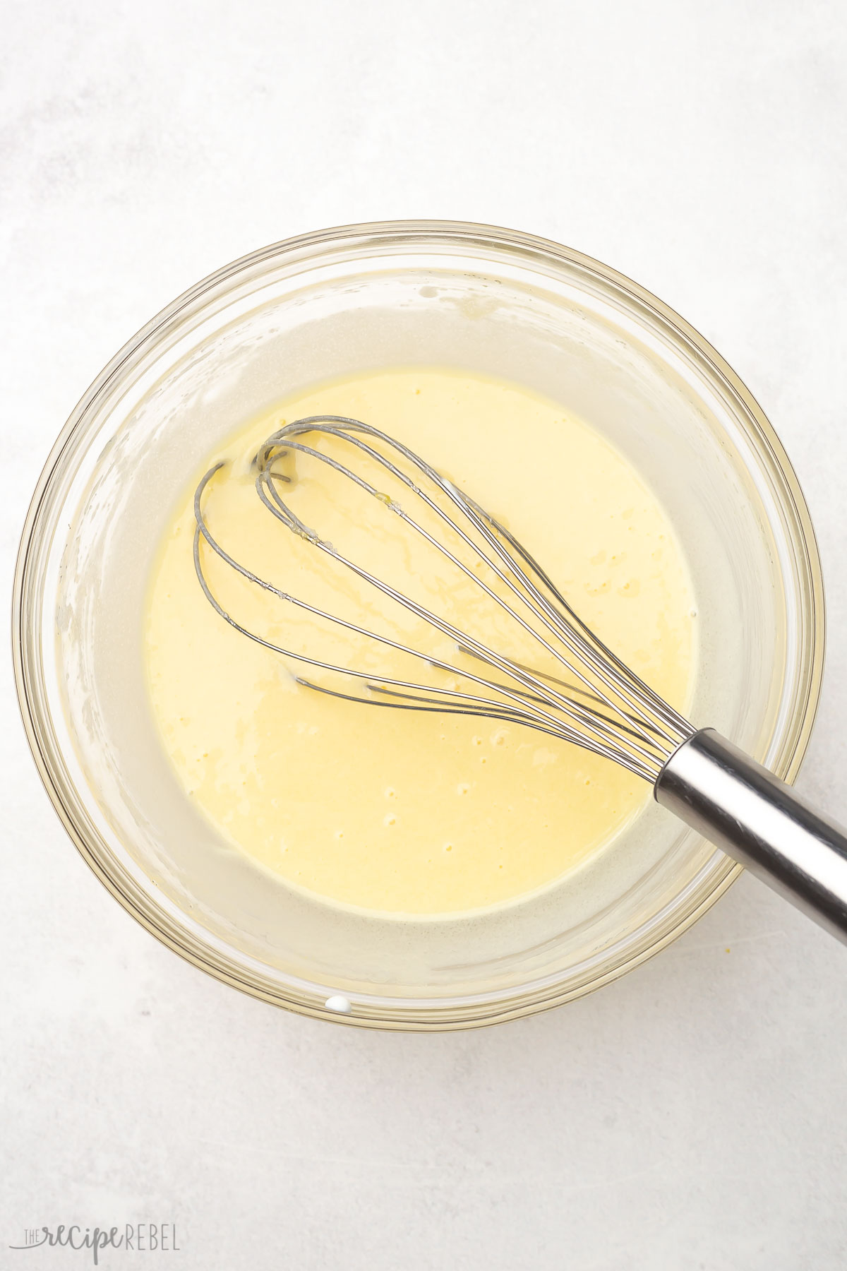 Top view of lemon bread wet ingredients mixed in a glass bowl with a steel whisk.