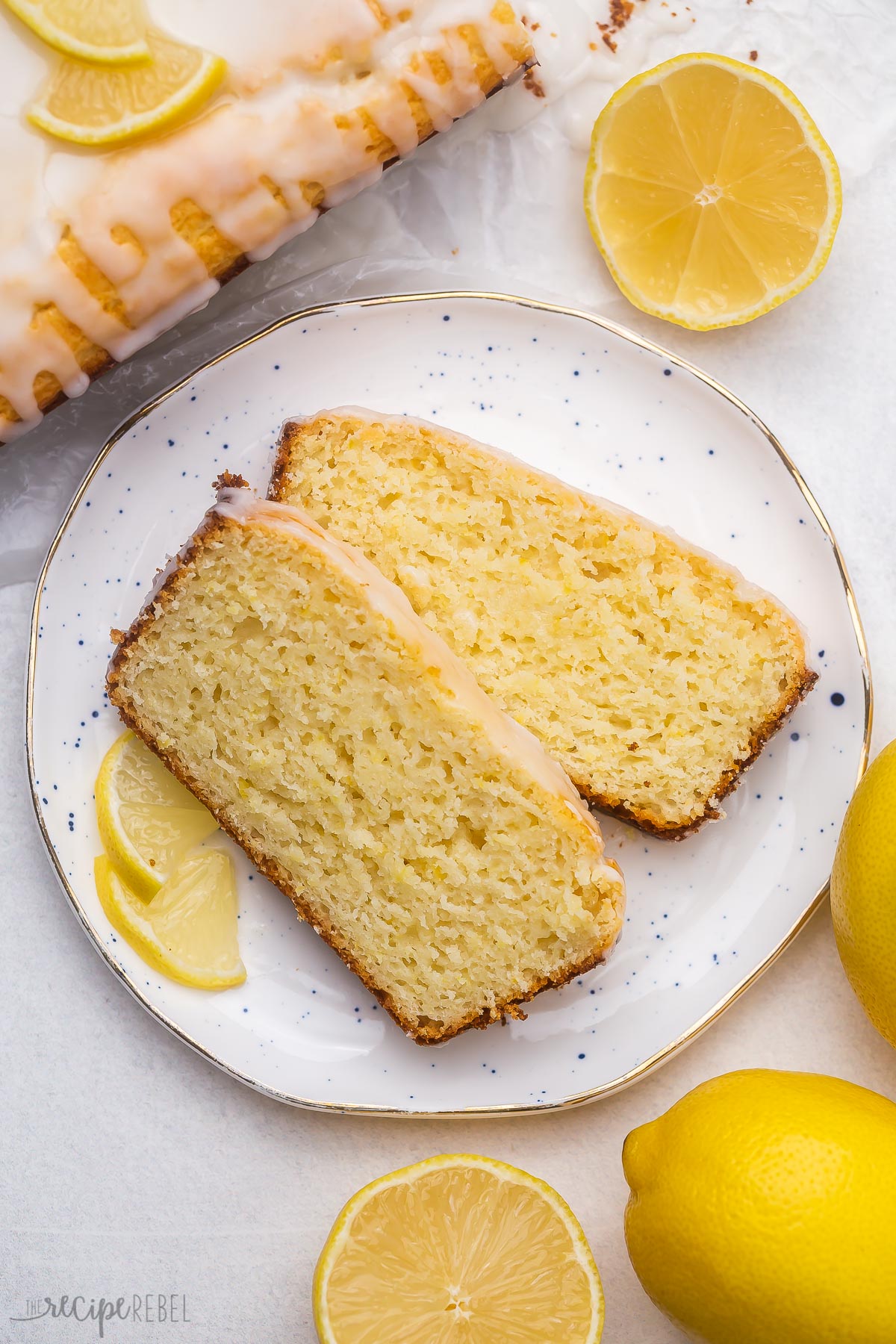 two slices of lemon bread on a white plate with lemons around it.