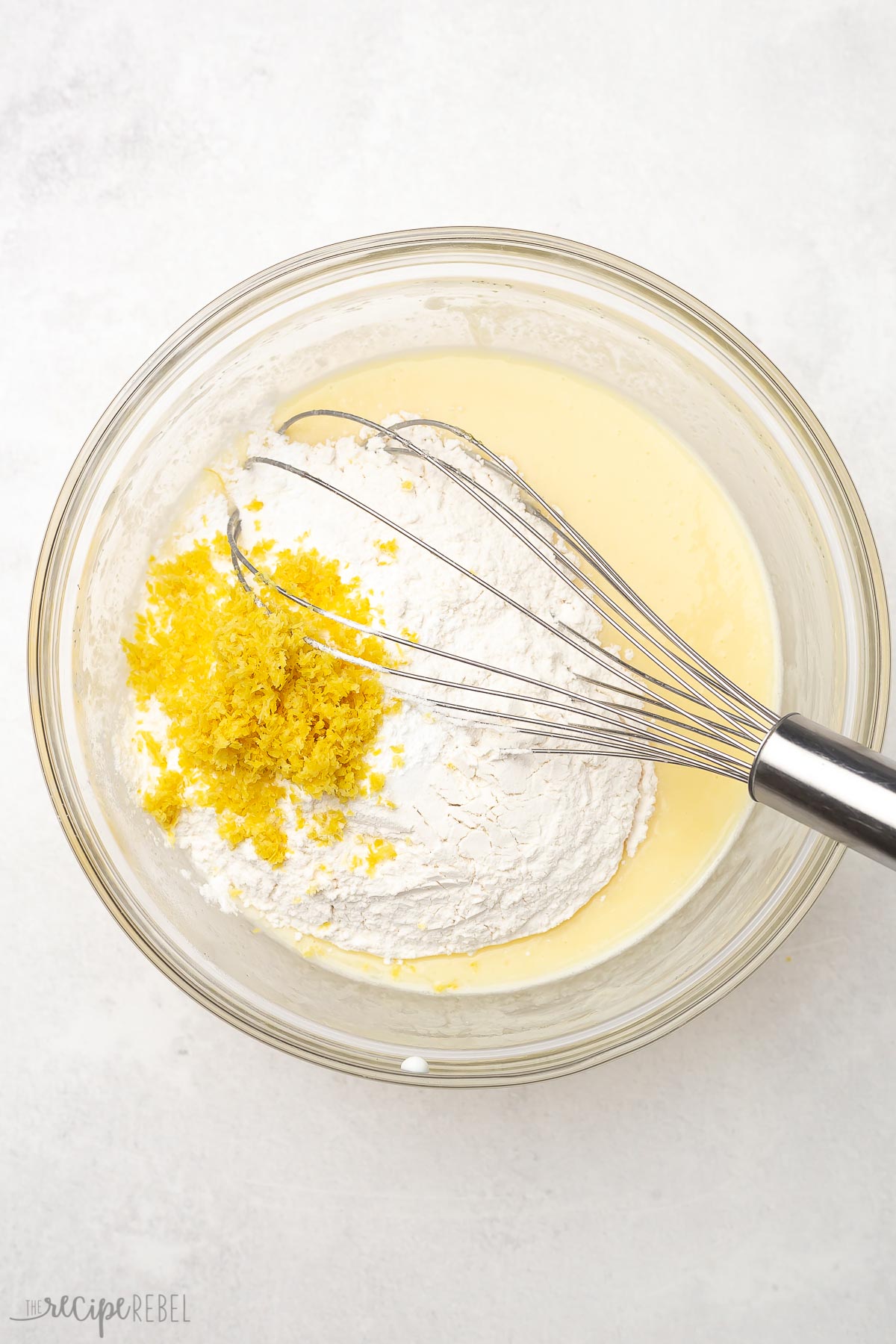 Top view of flour, baking powder, salt, and lemon zest added to bowl with other mixed ingredients.