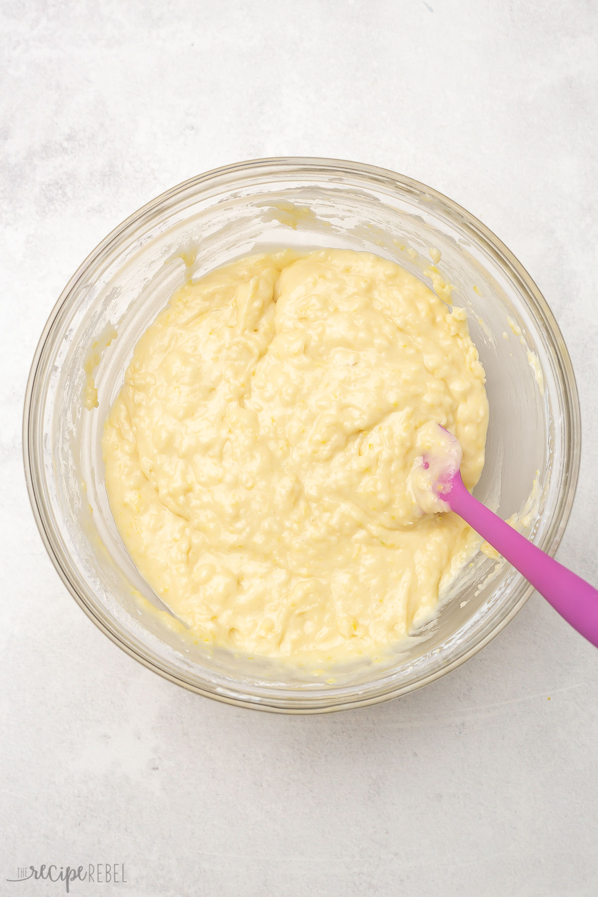 Top view of bowl of mixed lemon bread ingredients in a glass bowl with a spatula.