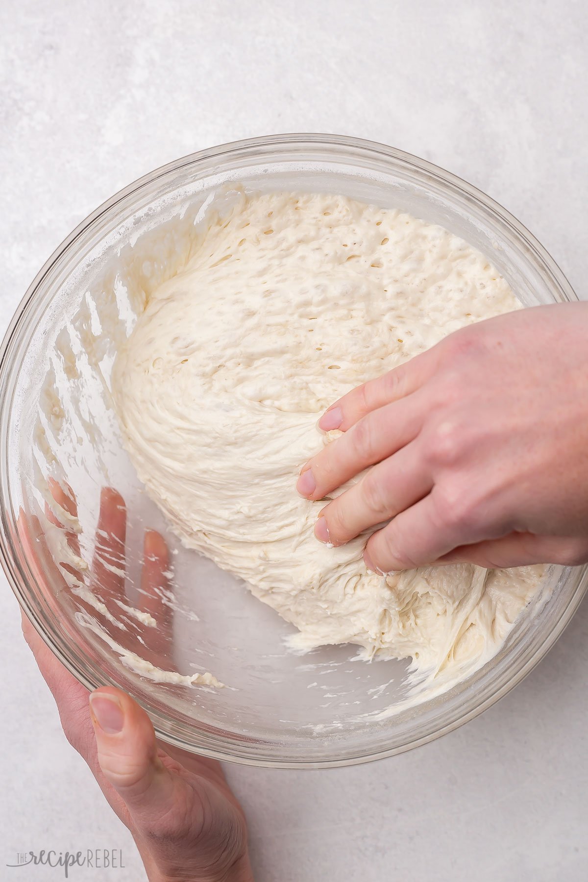 hands in a glass bowl pulling the sticky dough.
