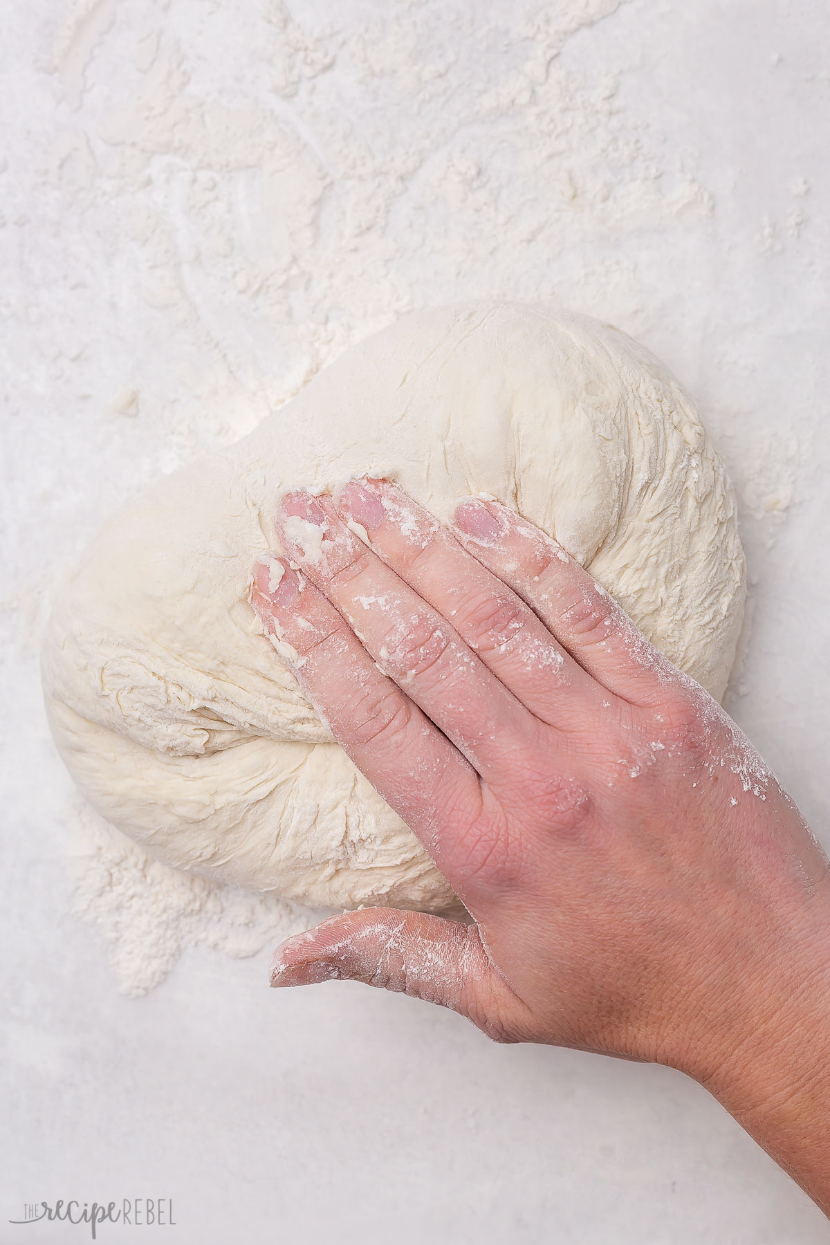 ball of dough on floured grey surface being rolled by hand.