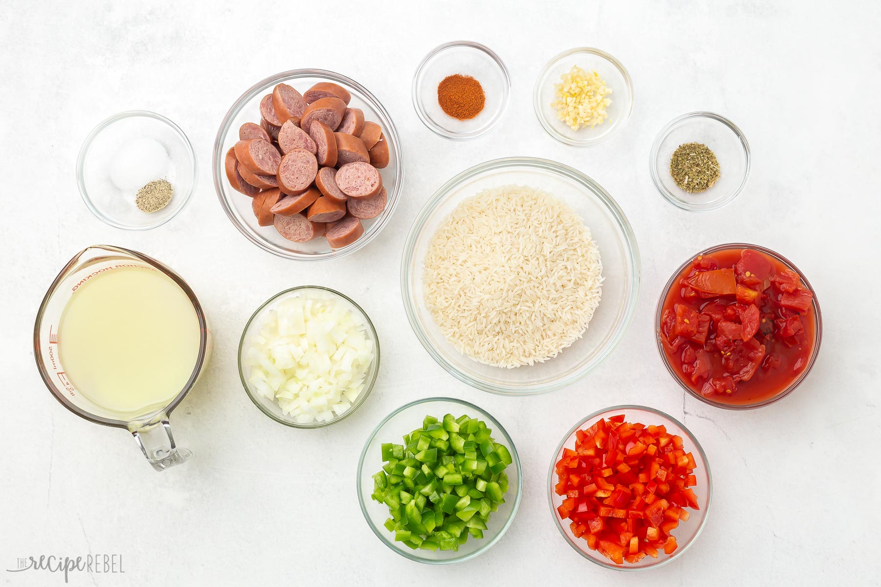 Overhead view of one pot sausage and rice ingredients in glass bowls.