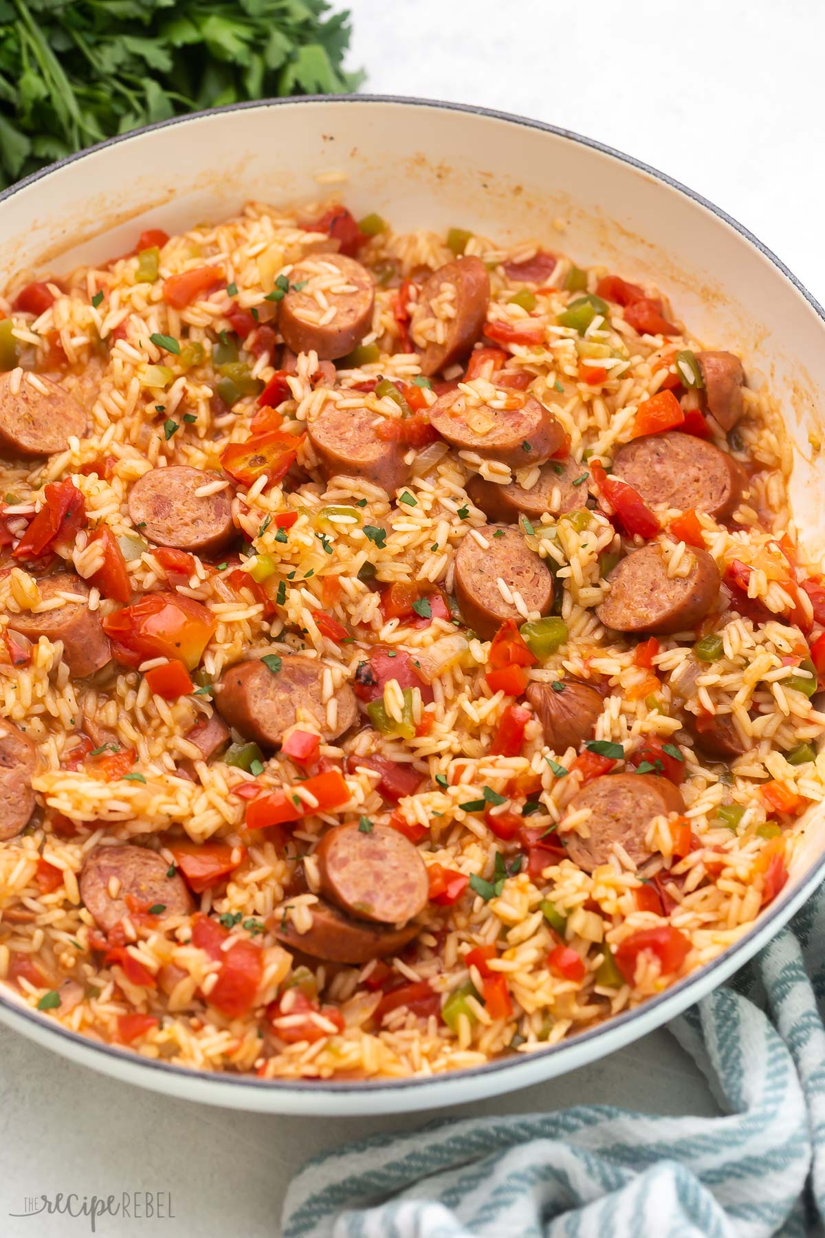 Top view of cooked one-pot sausage and rice in a white pan with parsley in the background.