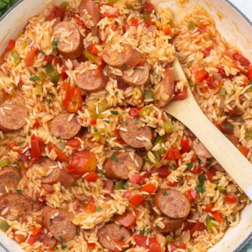 overhead shot of cooked one pan sausage and rice with wooden ladle.
