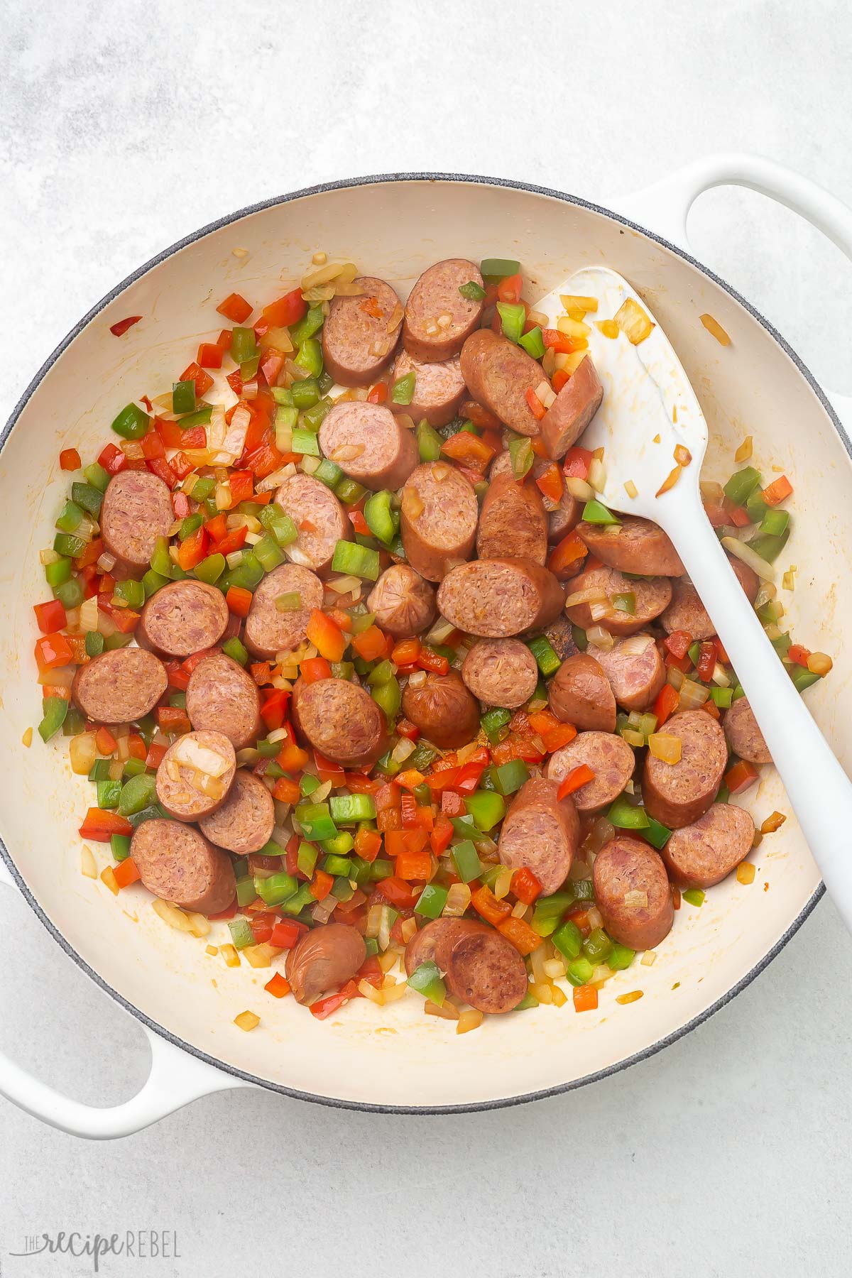 white ladle and pot full of sausage and and vegetables.