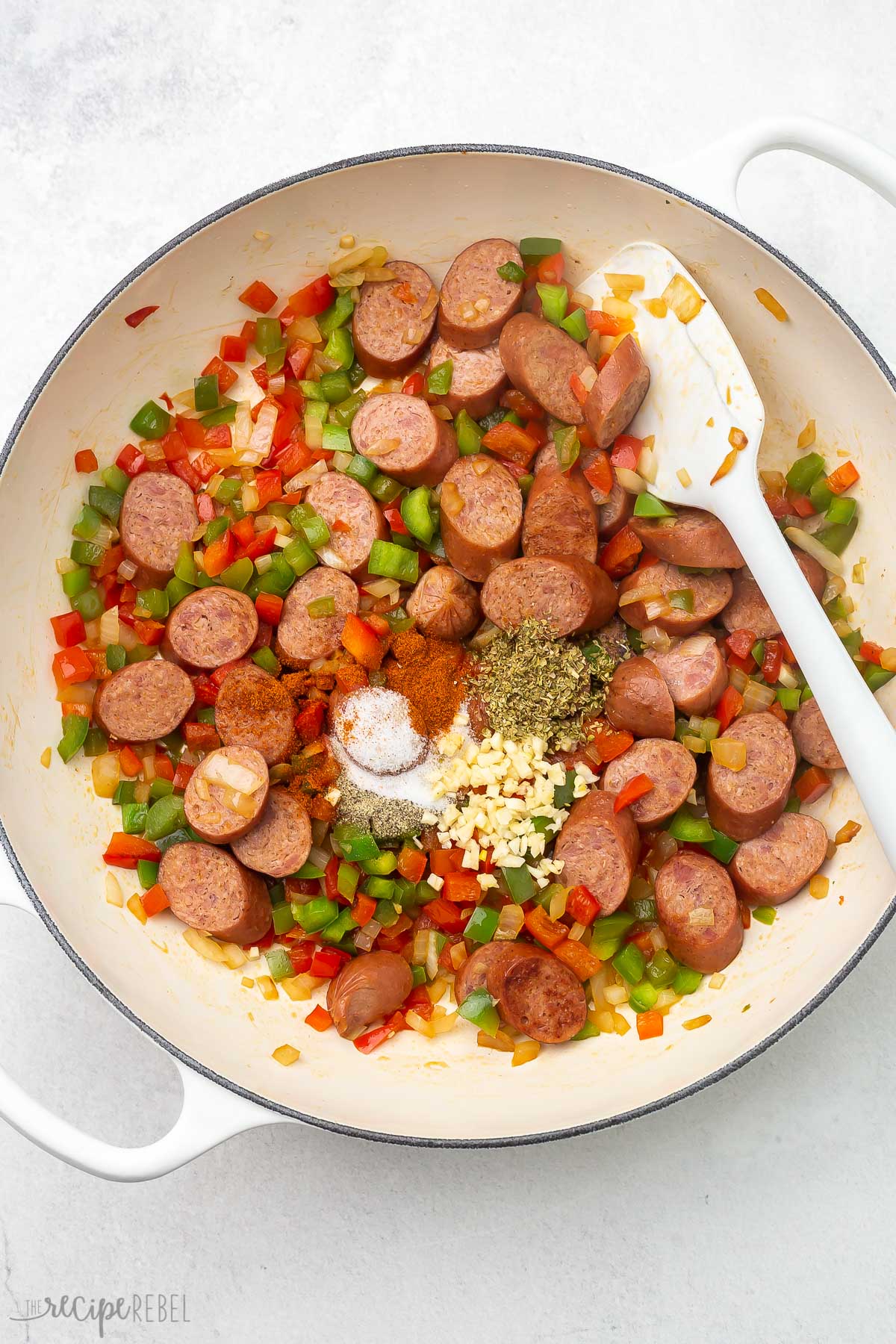 sauteed vegetables, sausage and spices in white pot.