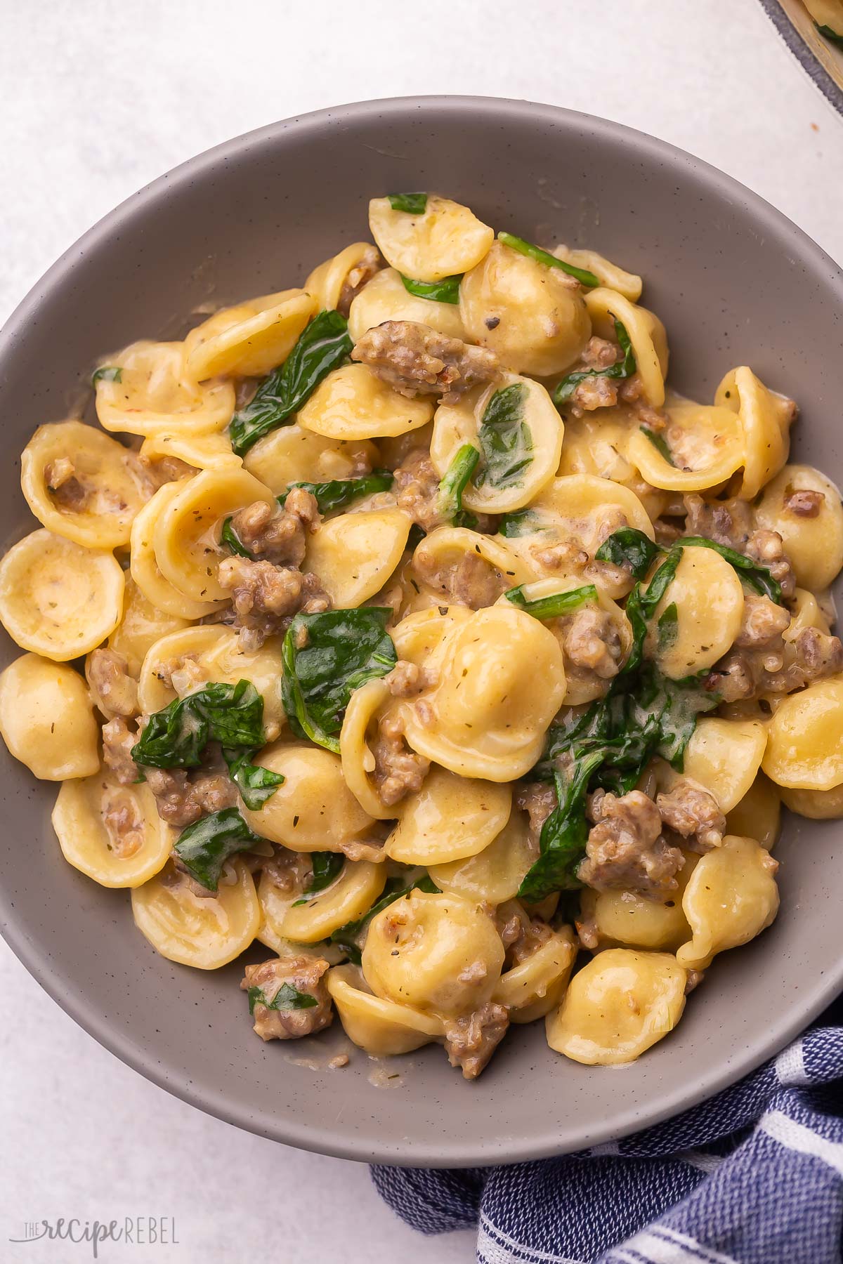 Close up of orecchiette pasta and sausage on a grey plate.