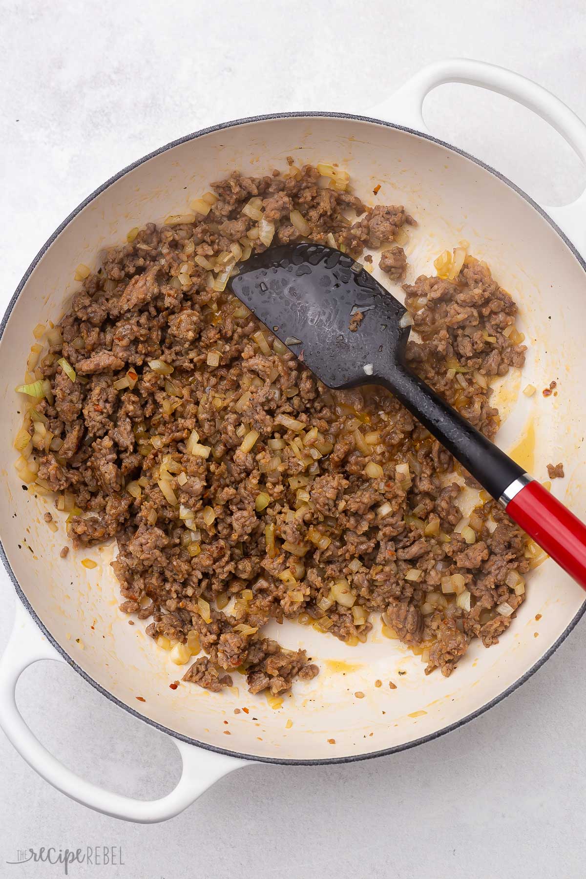 cooked ground sausage and red ladle in pan.