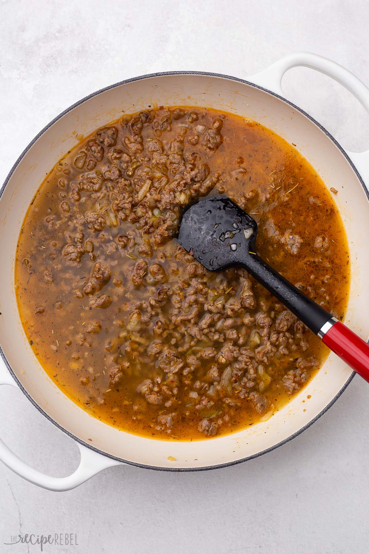 overhead view of cooked sausage, spices, and broth in white pot.