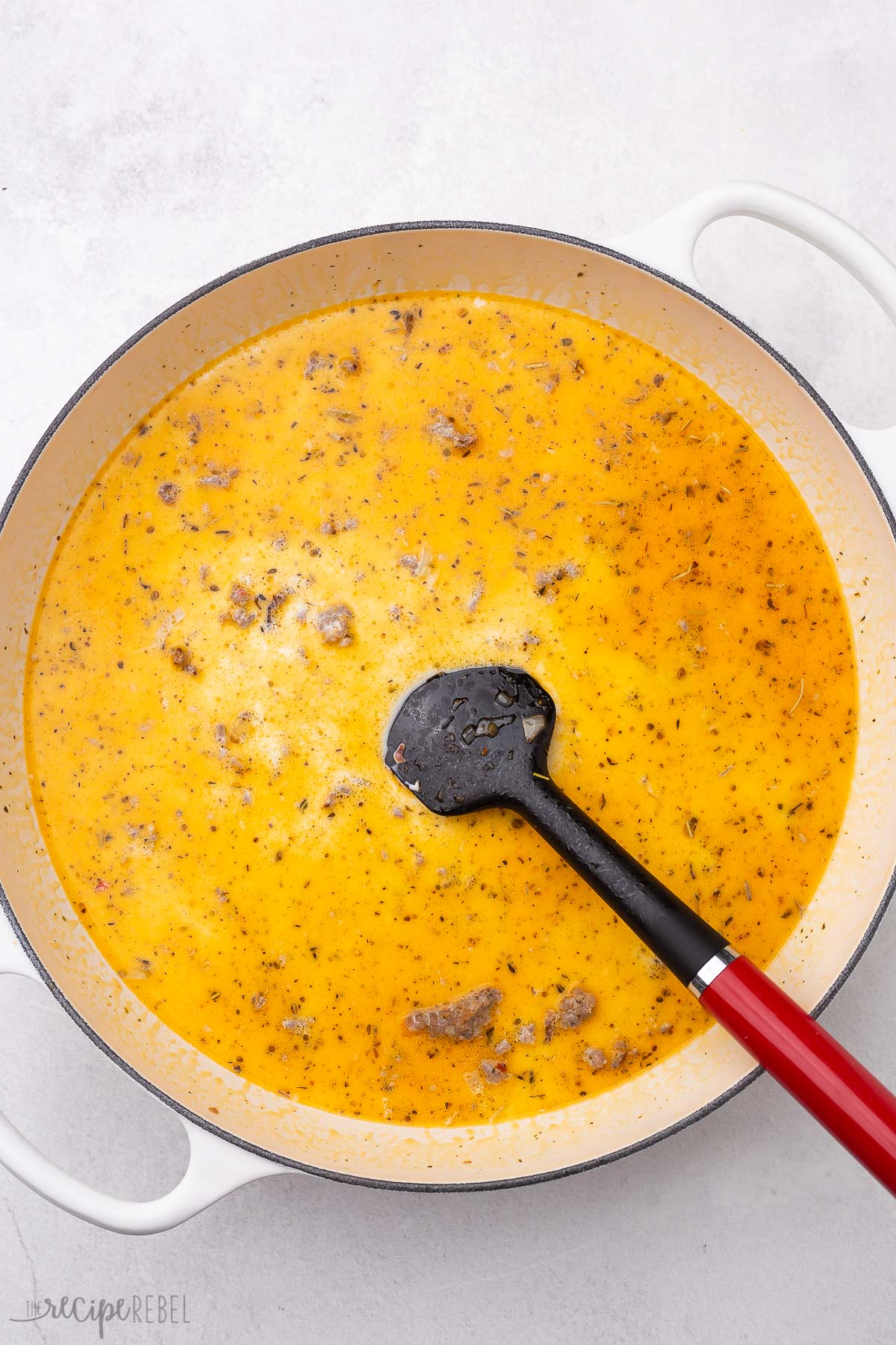 cream added to white pot of ingredients for orecchiette pasta with sausage.