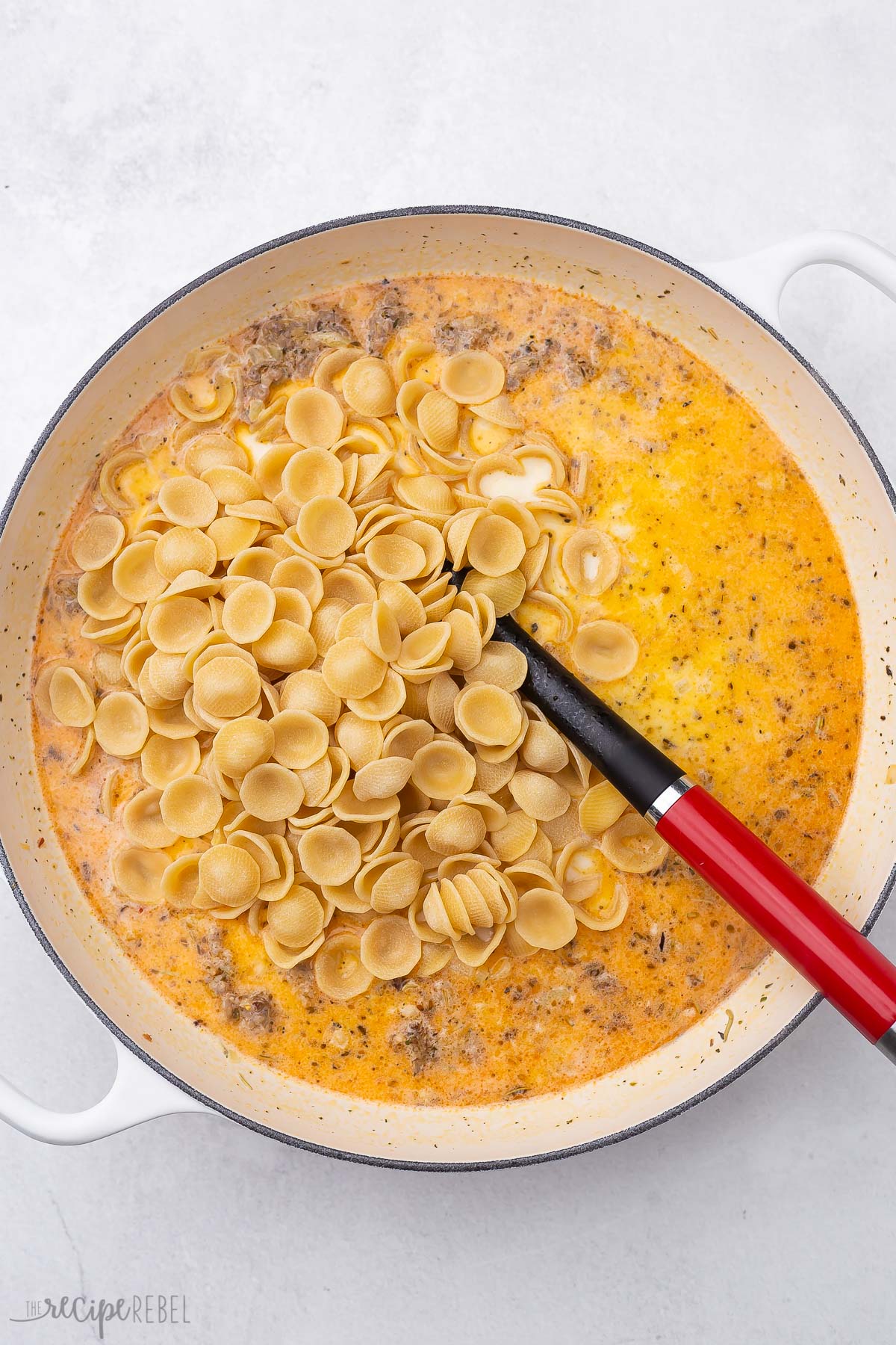 orecchiette pasta added on top of ingredients in white pot.