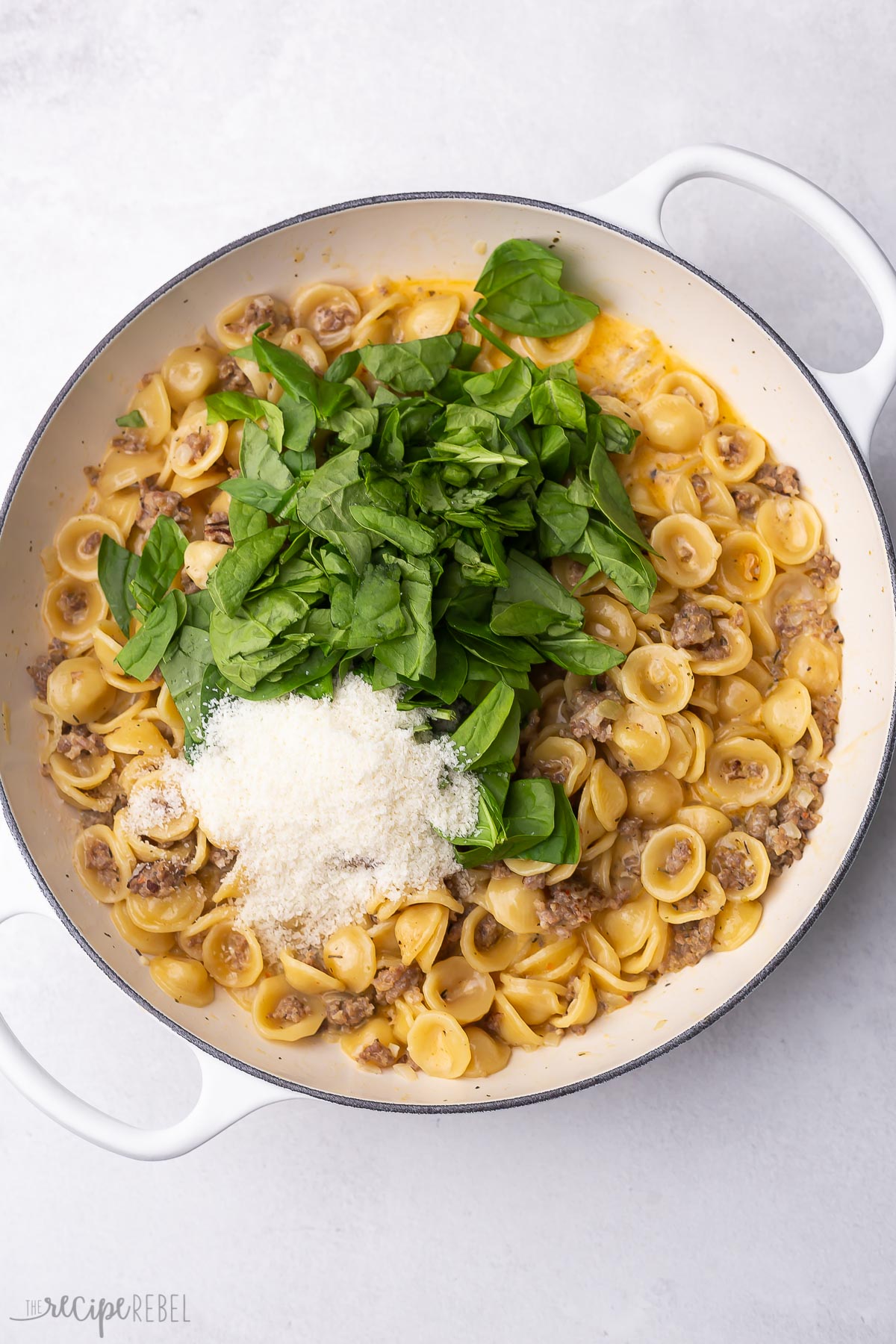 cooked pot of orecchiette pasta and sausage with spinach and cheese add on top.