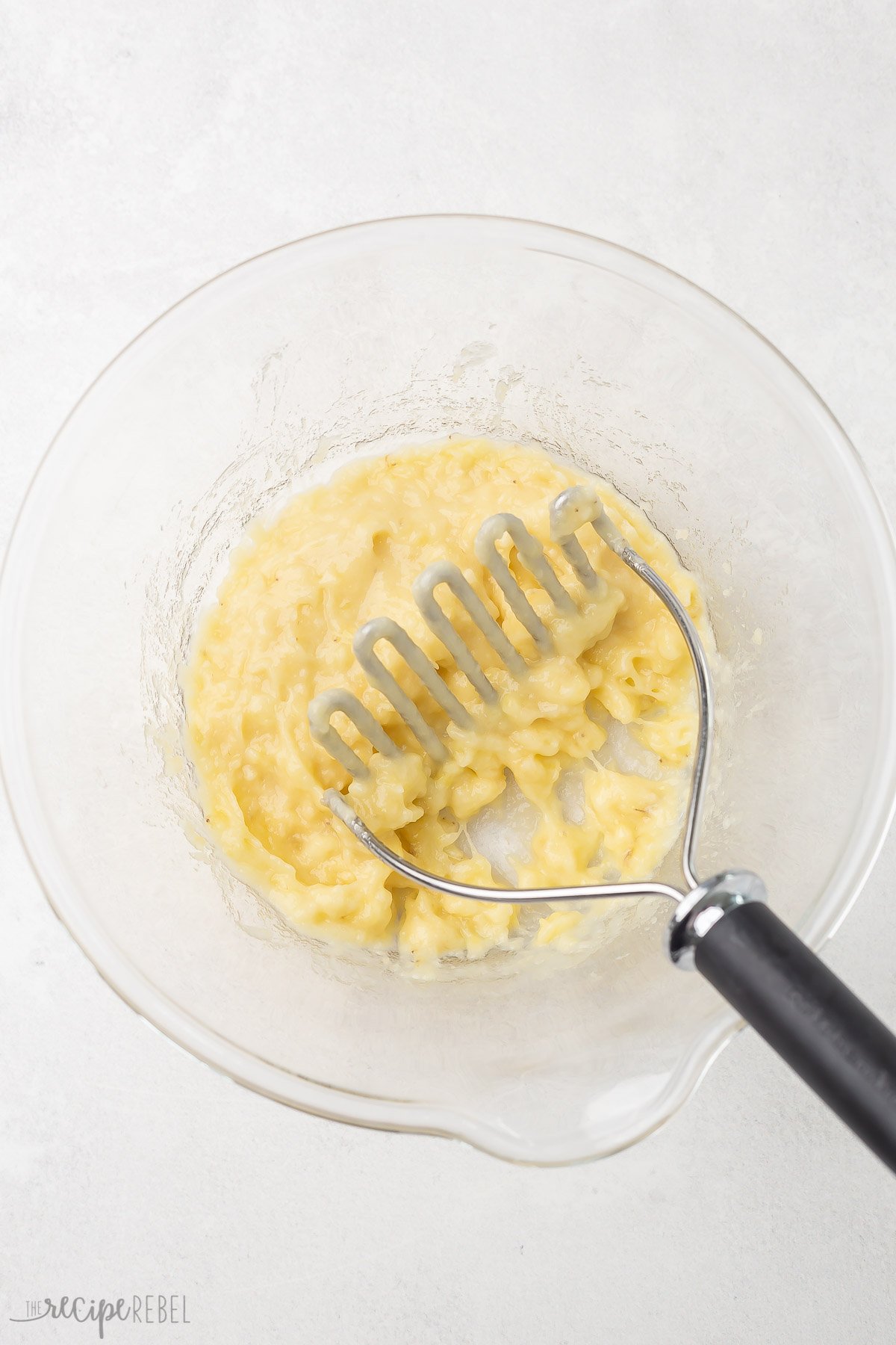 glass bowl with mashed bananas on grey surface.