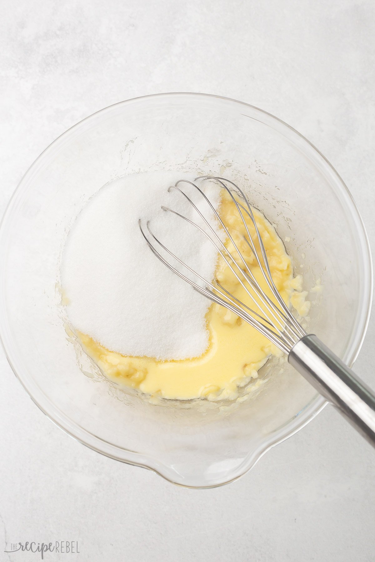 glass bowl with mashed bananas, sugar, and steel whisk.