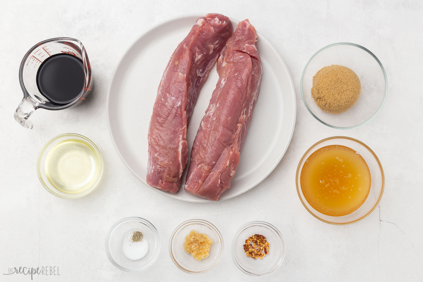 overhead view of pork tenderloin marinade ingredients in glass bowls on a grey surface.