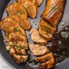 slices of cooked pork tenderloin lying in black pan with sauce.