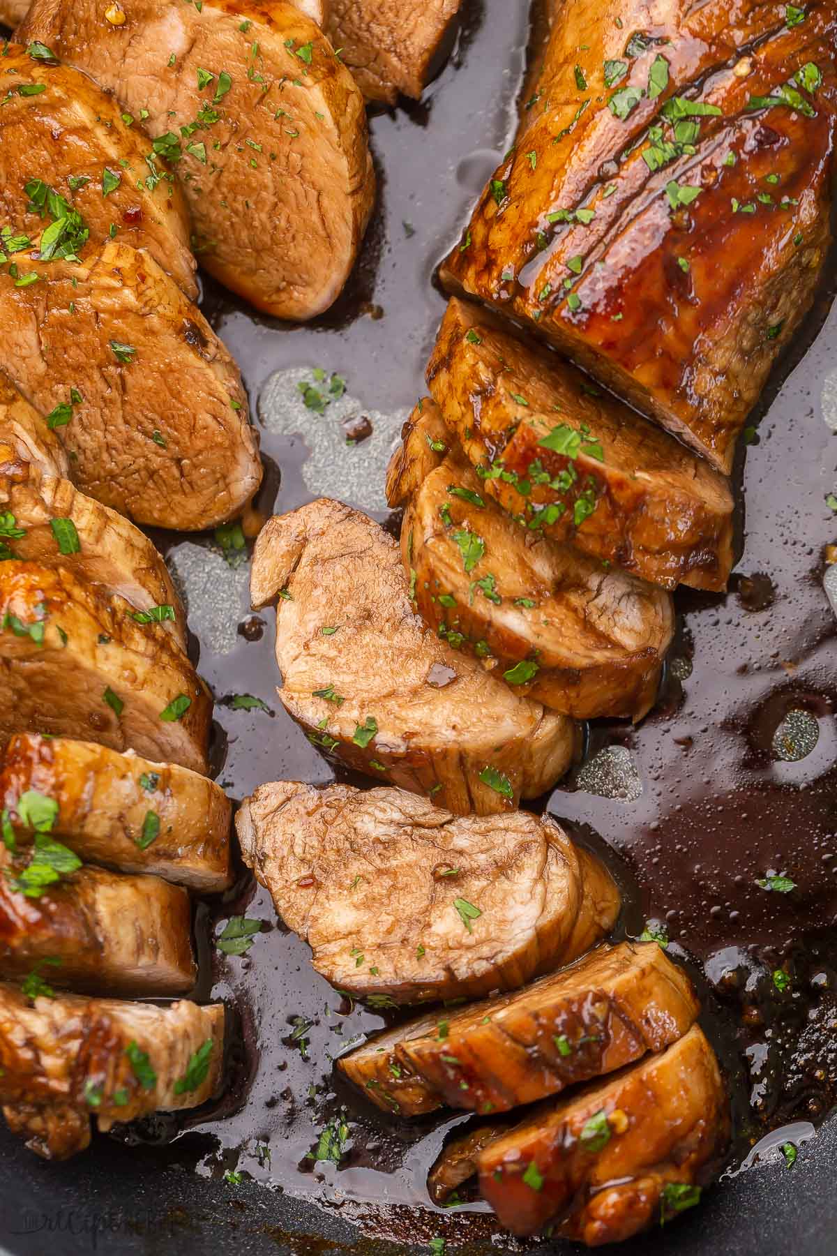 Top view close up of sliced pork tenderloin in black pan with sauce.