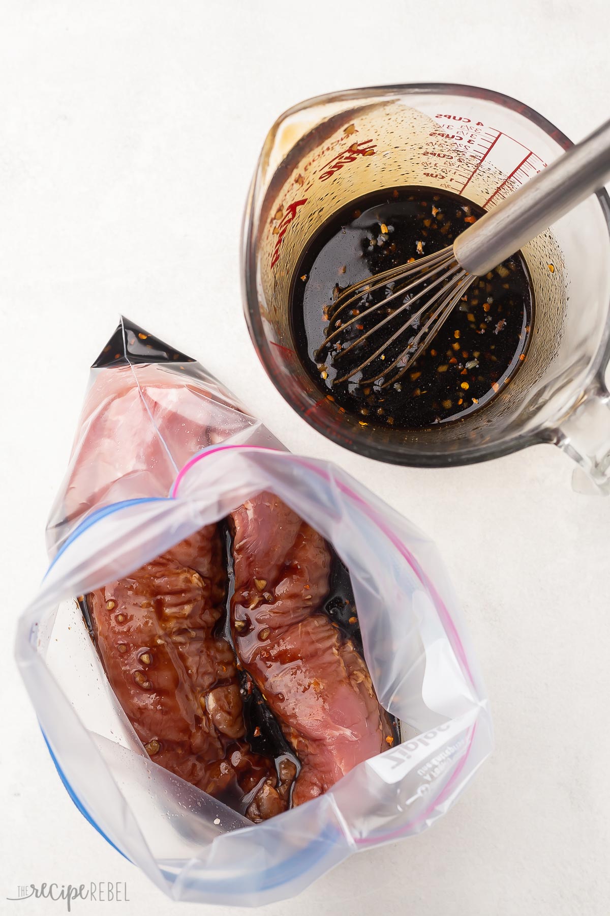 zipper seal bag with pork tenderloin and marinade with extra marinade in measuring cup beside.