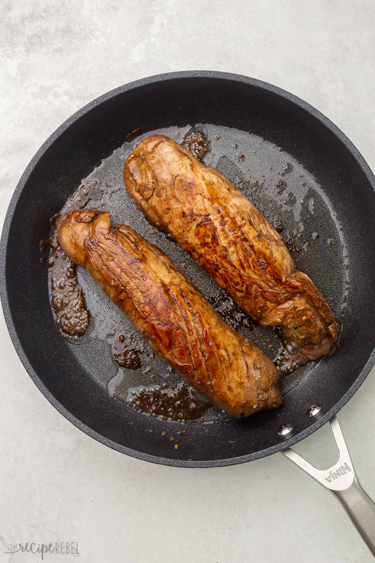 overhead shot of pork tenderloin cooked in a black frying pan.