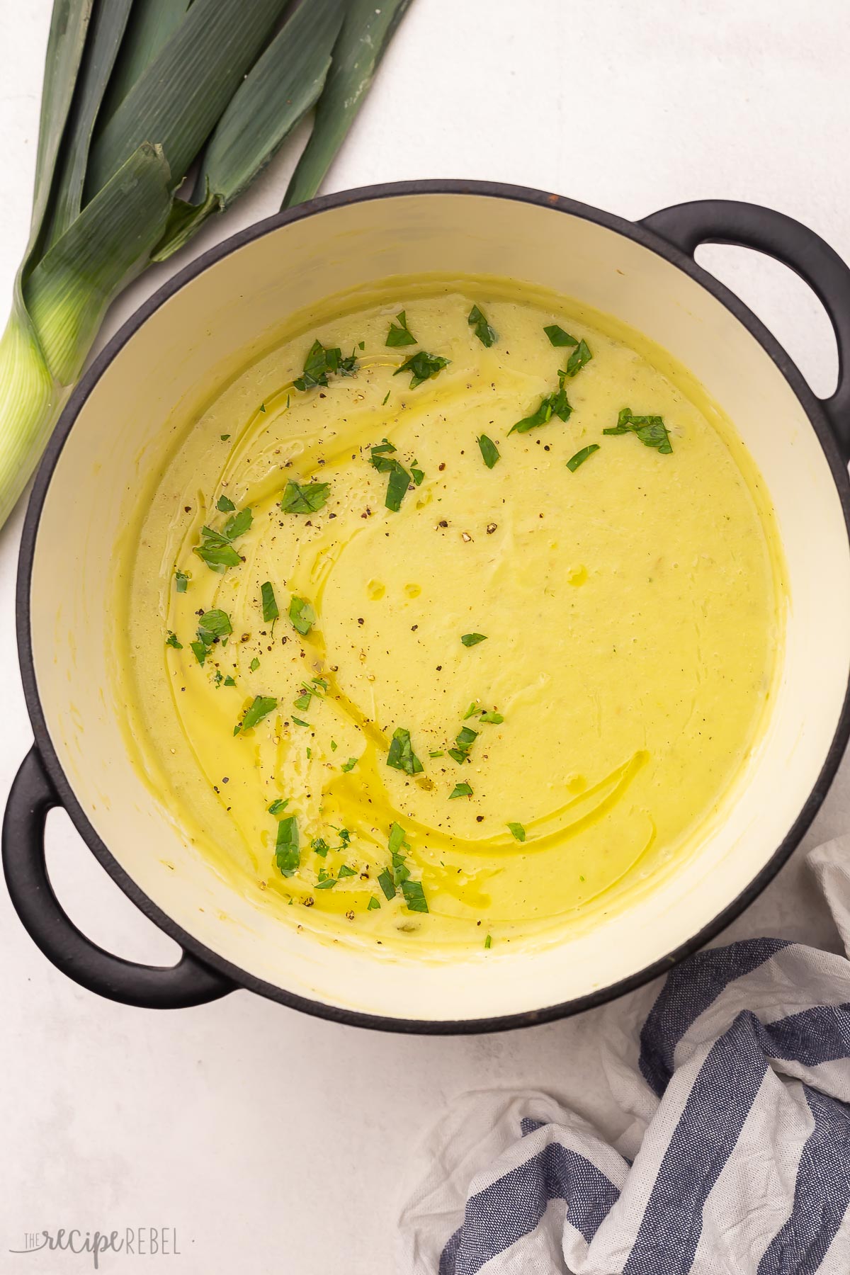 a large pot of potato leek soup on a grey surface with leeks lying beside it.