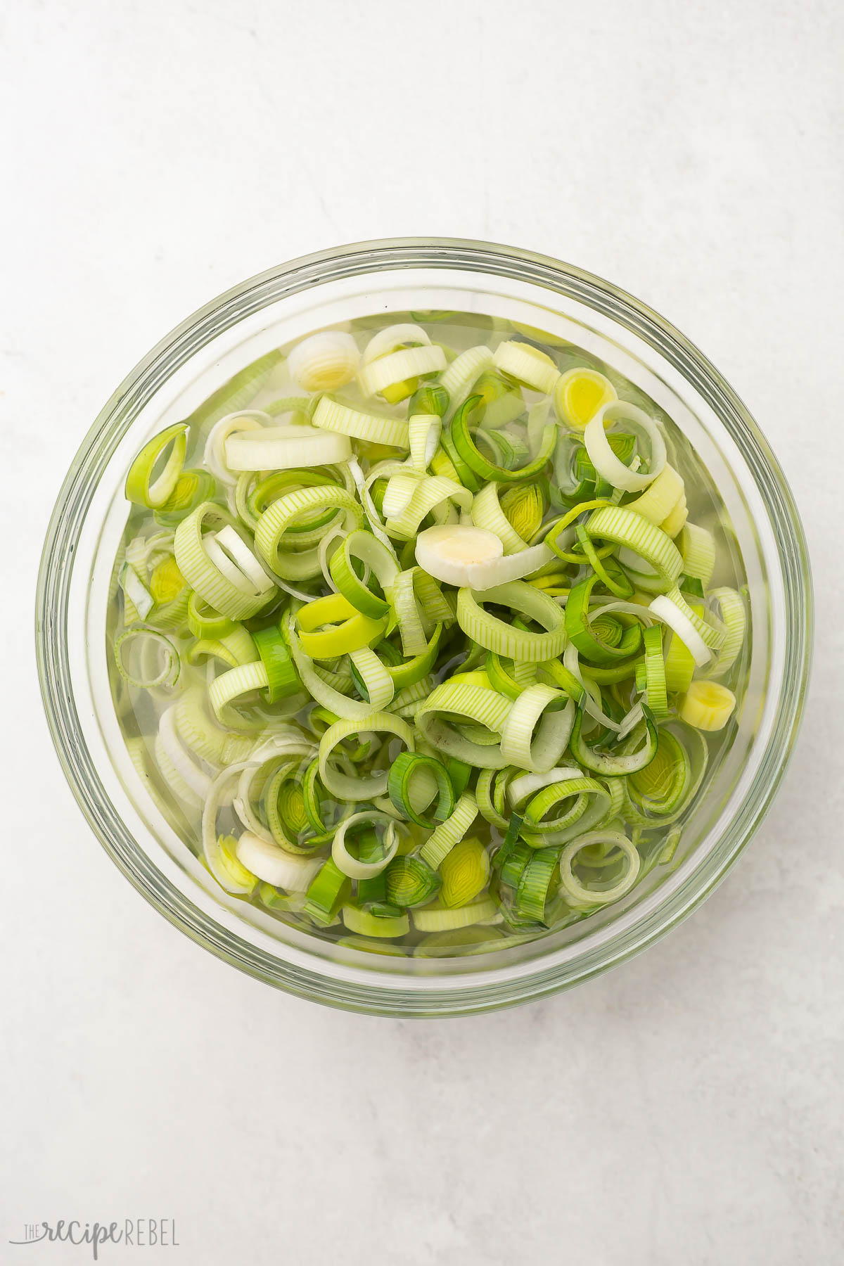 a glass bowl of chopped leeks on a grey surface.