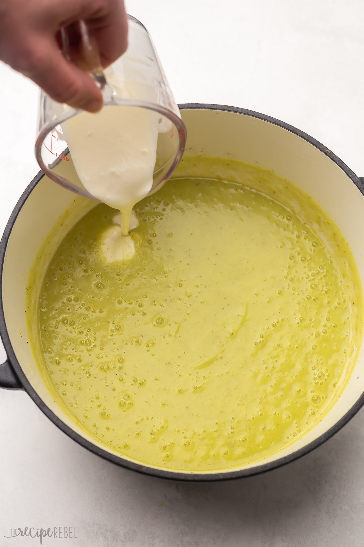 hand pouring cream into pot of potato leek soup.