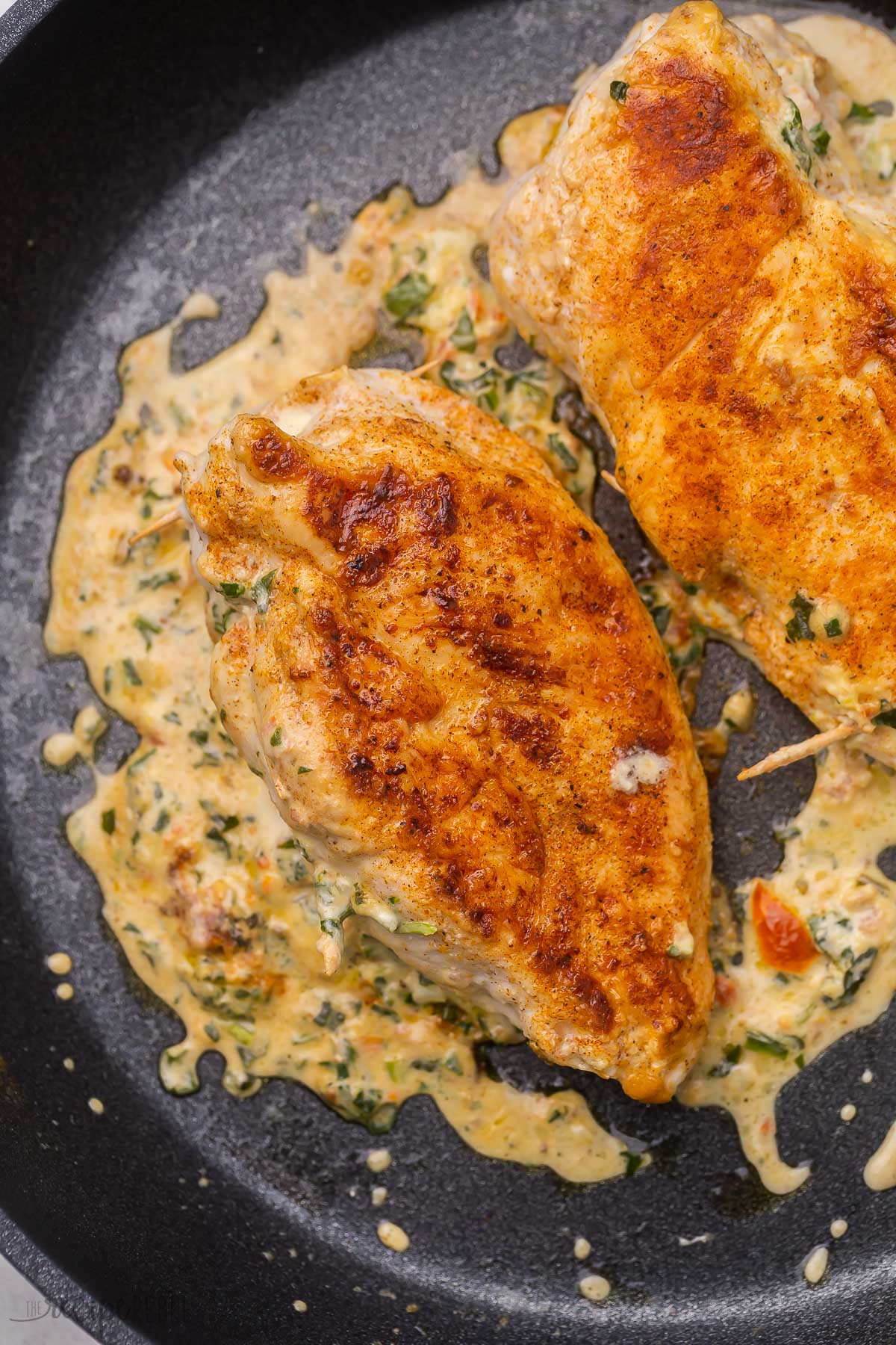 cooked spinach stuffed chicken breasts lying in a frying pan.