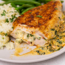 Close up of a cut open chicken breast on a white plate with rice and green beans around it.