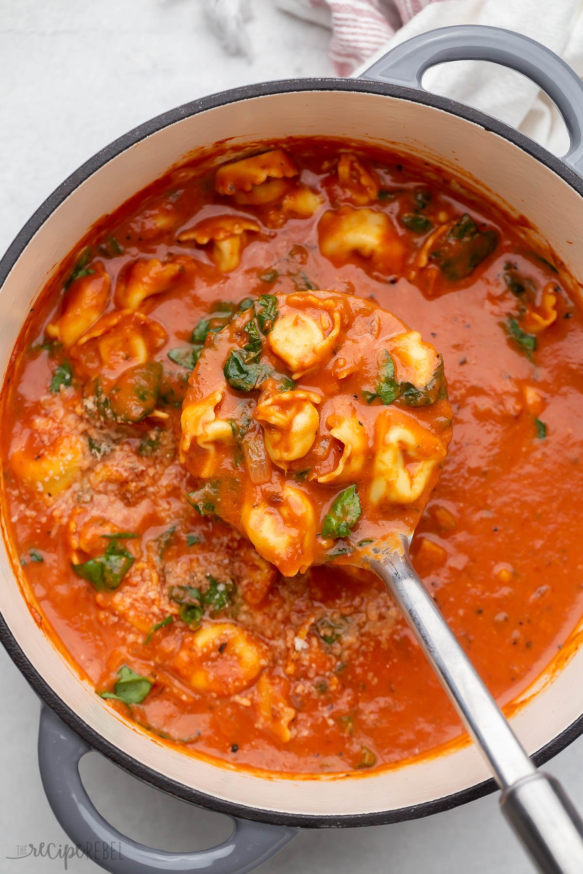 overhead image of a pot of tomato tortellini soup with ladle.