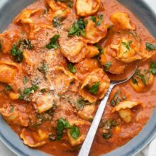 tomato tortellini soup in a blue bowl with a spoon.