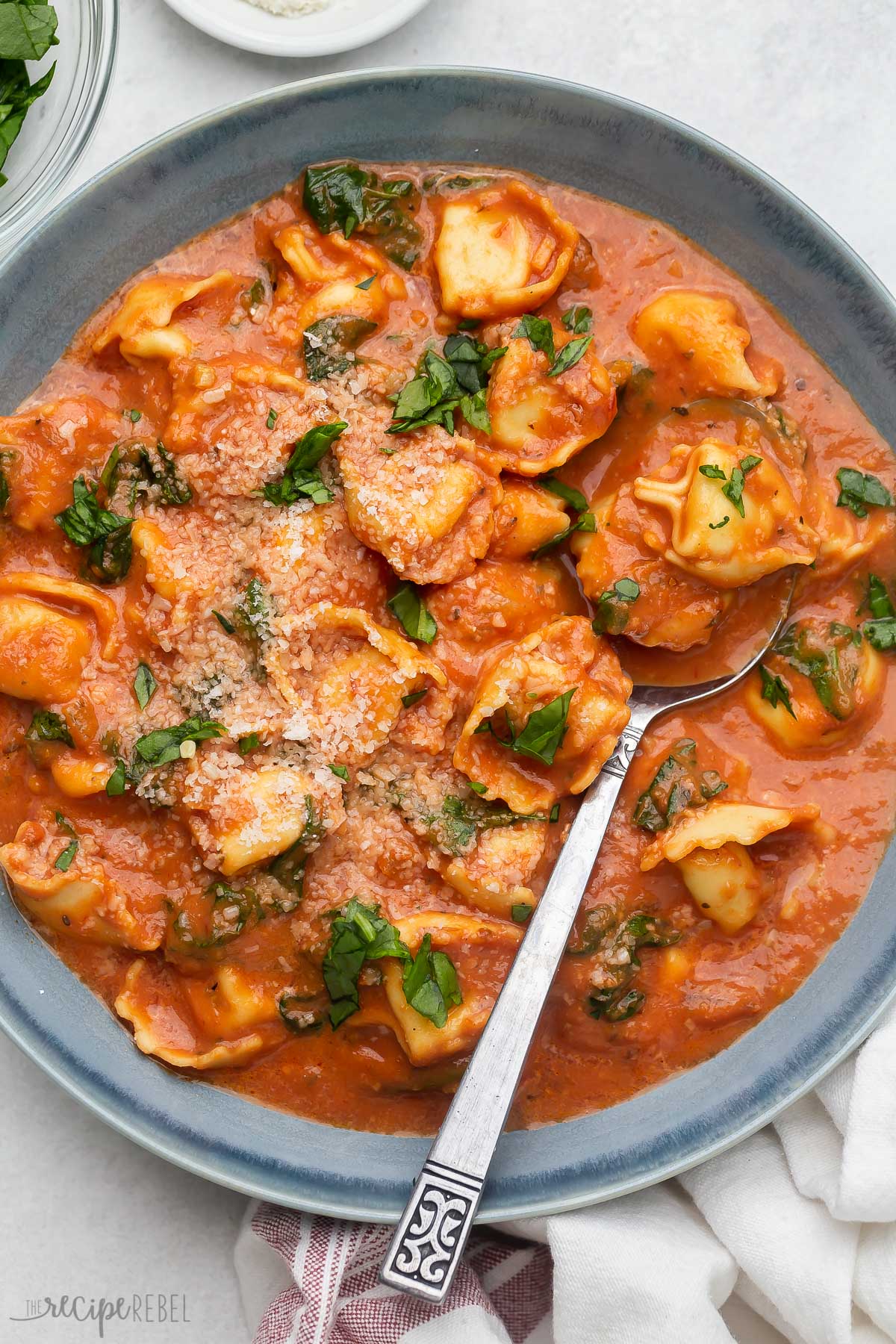 tomato tortellini soup in a blue bowl with a spoon.