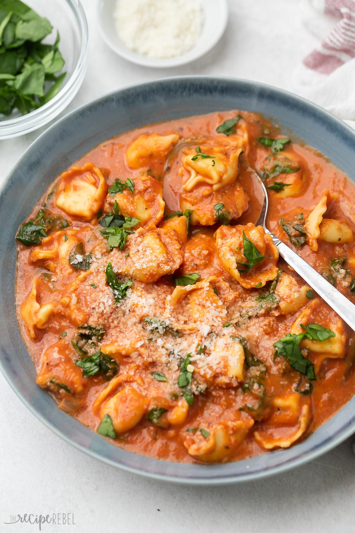 a blue bowl with tomato tortellini soup and a spoon in it.