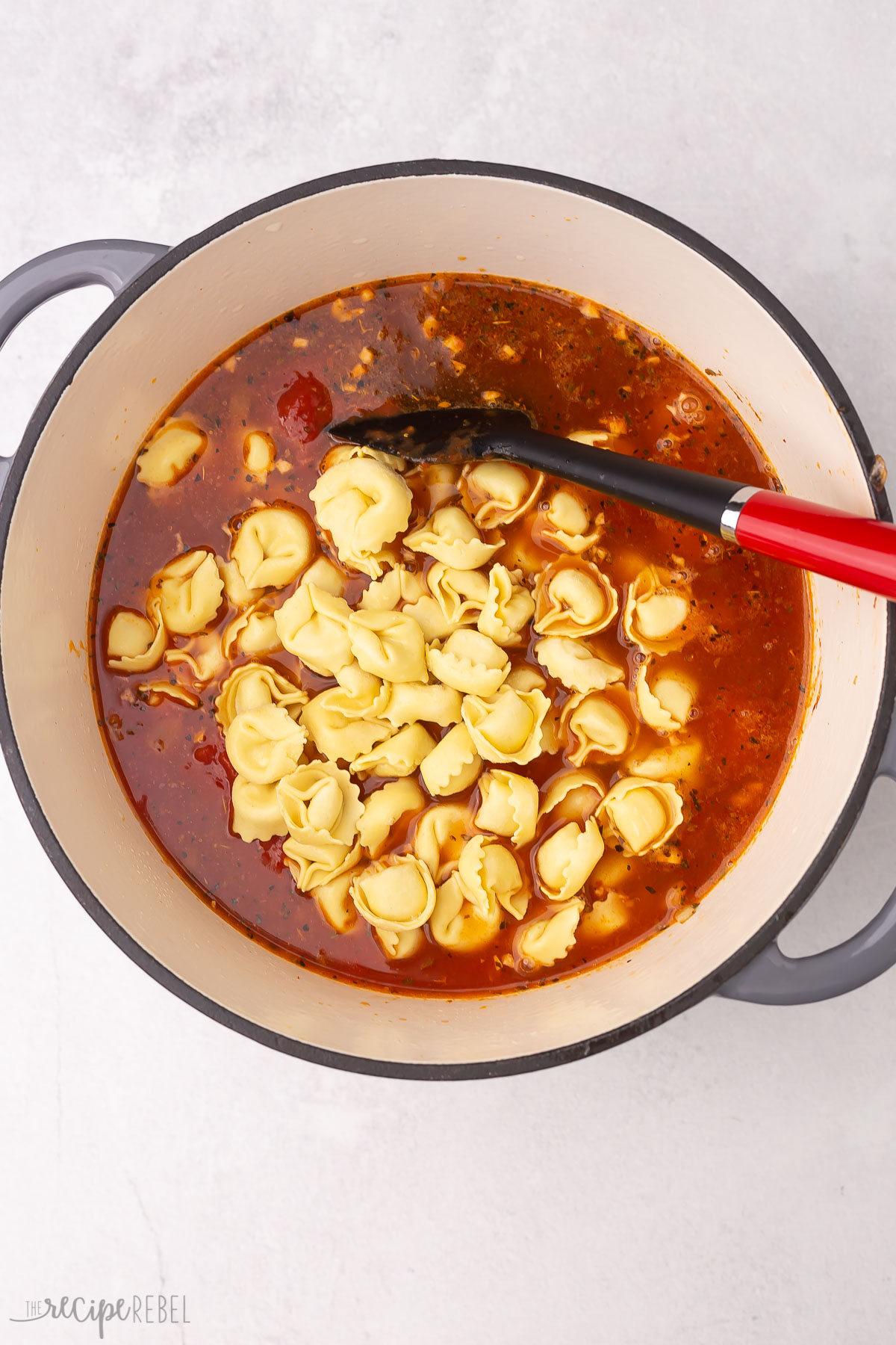 tortellini in dutch oven with red spatula.
