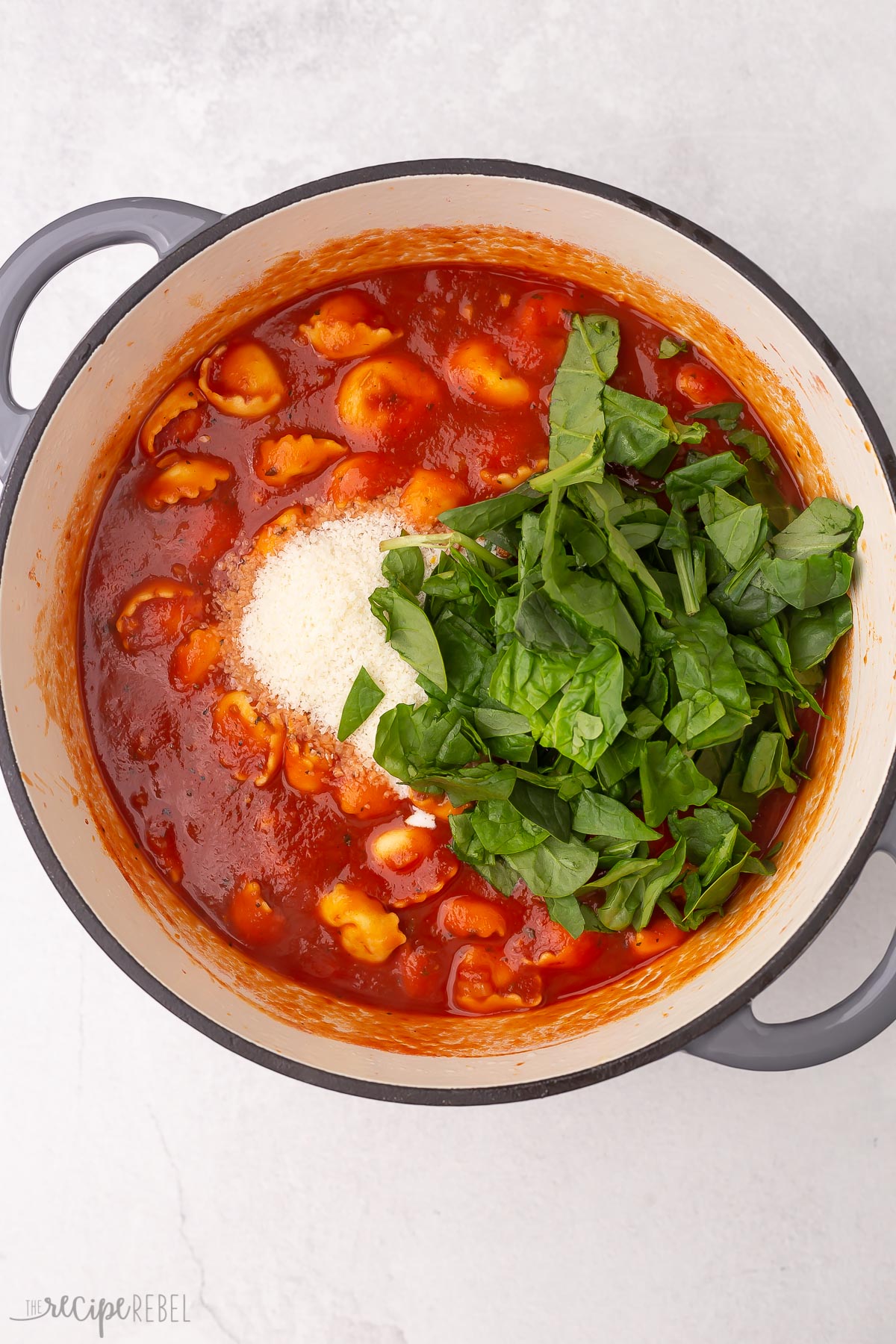 chopped spinach on top of tomato tortellini soup in pot.