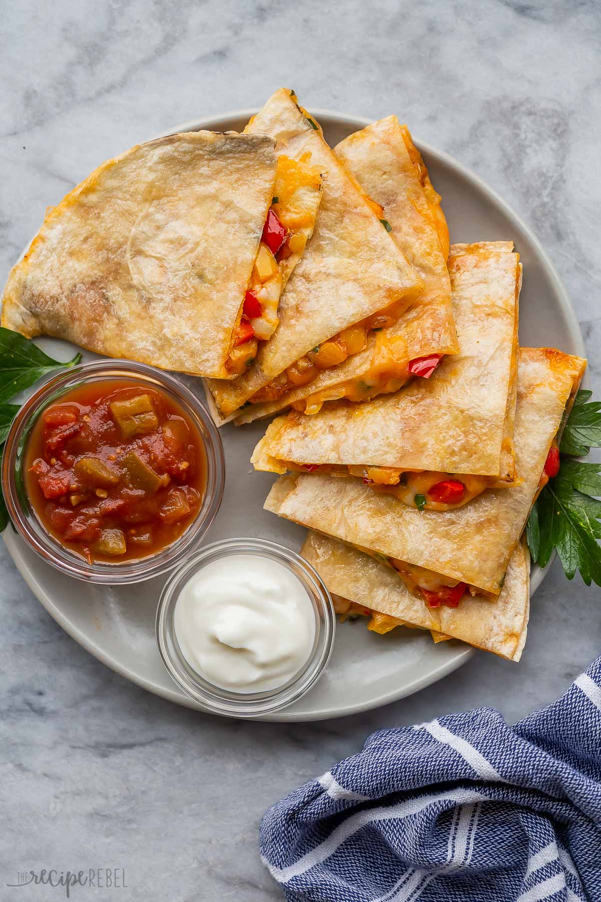Top view of quesadillas slices on a plate with glass bowls of sour cream and salsa.