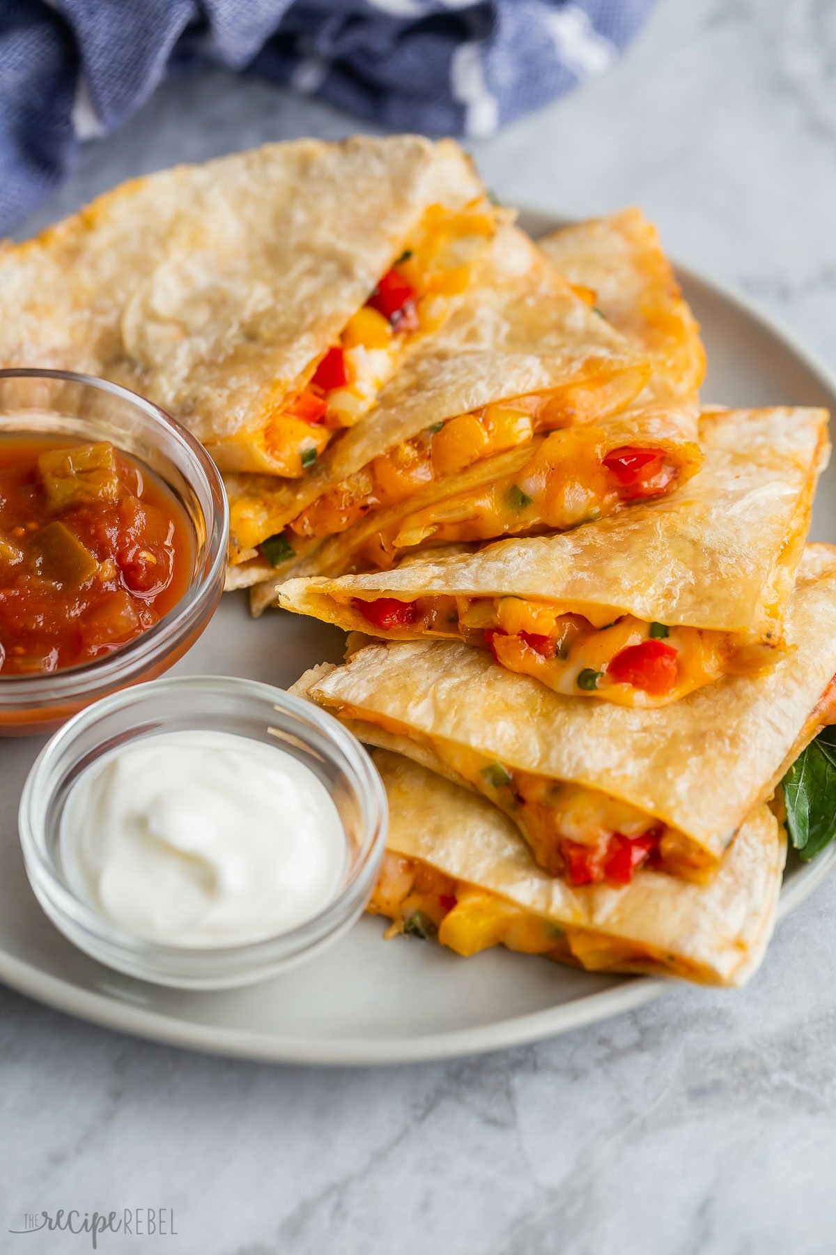 Slices of quesadilla stacked on plate with a bowl of sour cream and salsa beside it.