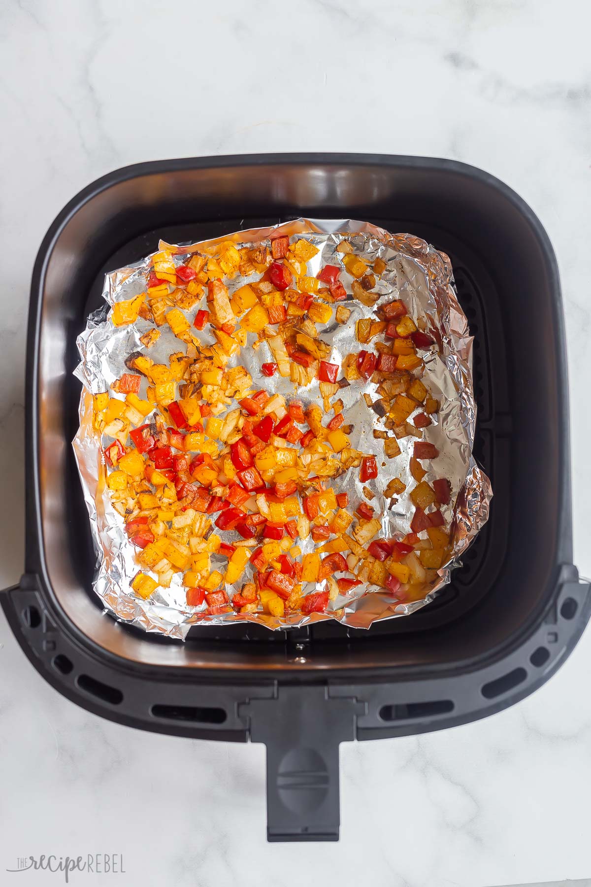 Sauteed red and yellow peppers on tinfoil in air fryer basket.