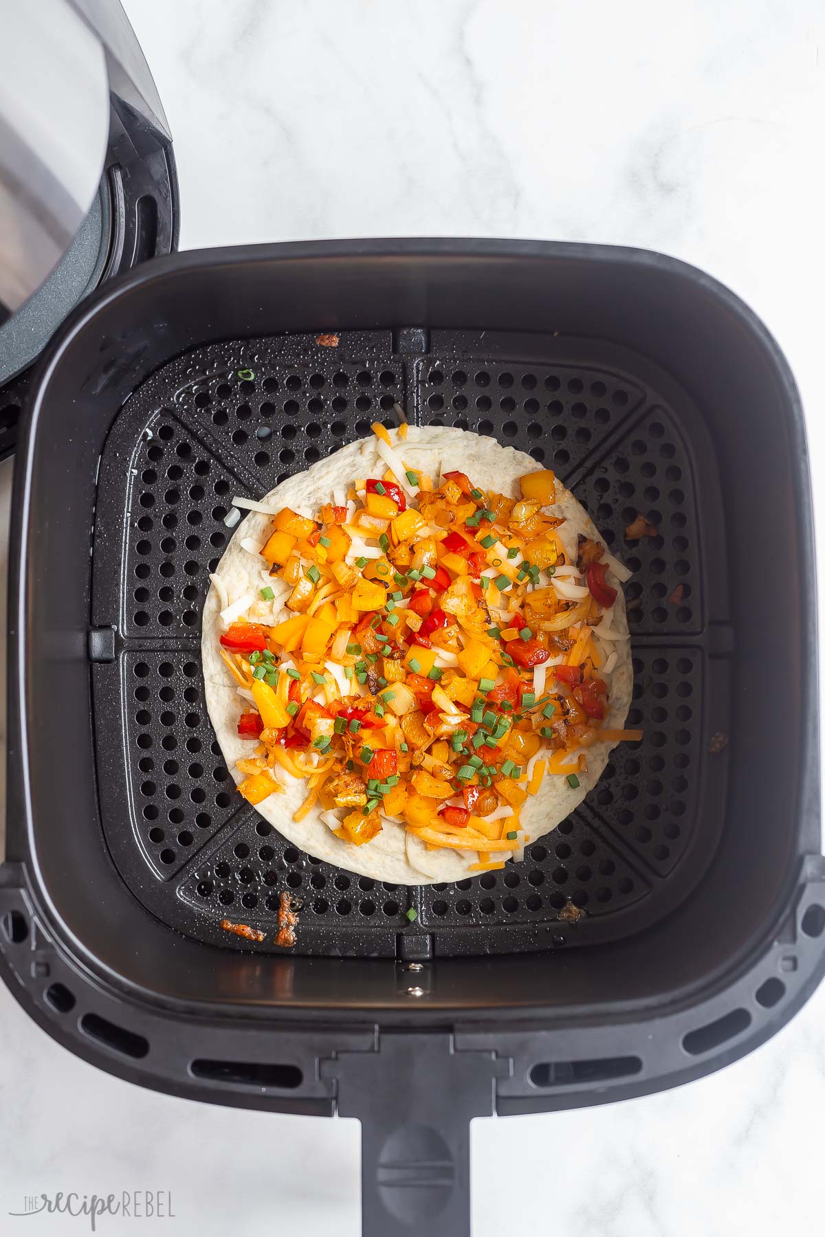 Top view of tortilla with toppings on it in air fryer basket.