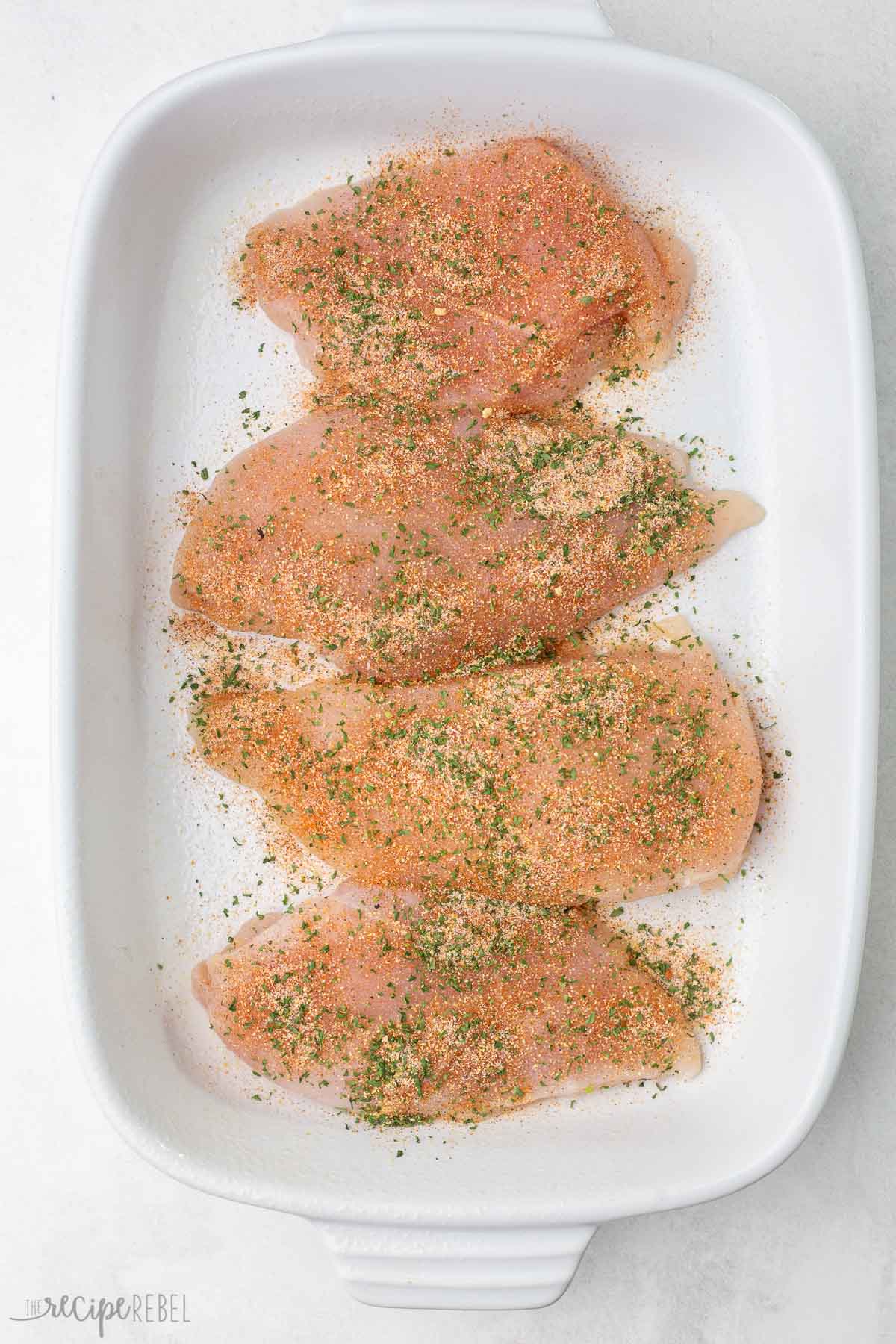 white baking dish with with seasoned chicken breasts inside.